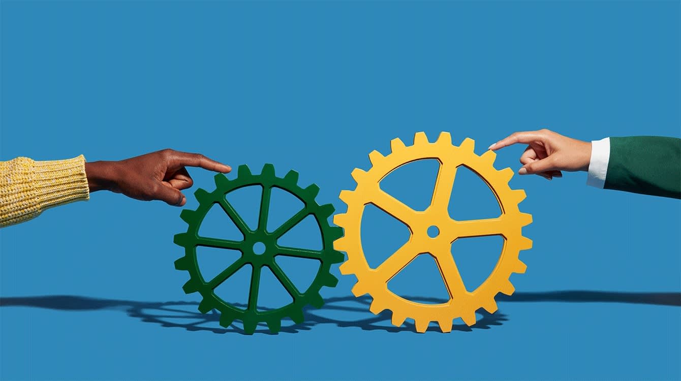 A green circular gear sits to the left of a yellow circular gear. Two hands try to move the gears from the left and right sides of the image.