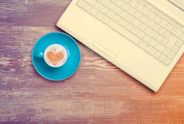 Image d’une tasse de café dans une soucoupe près d’un ordinateur portable. Il s’agit d’un délicieux café à la crème saupoudré de cannelle en forme de cœur.