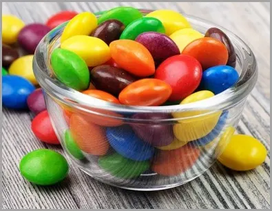 Colorful candy in and around a small glass bowl