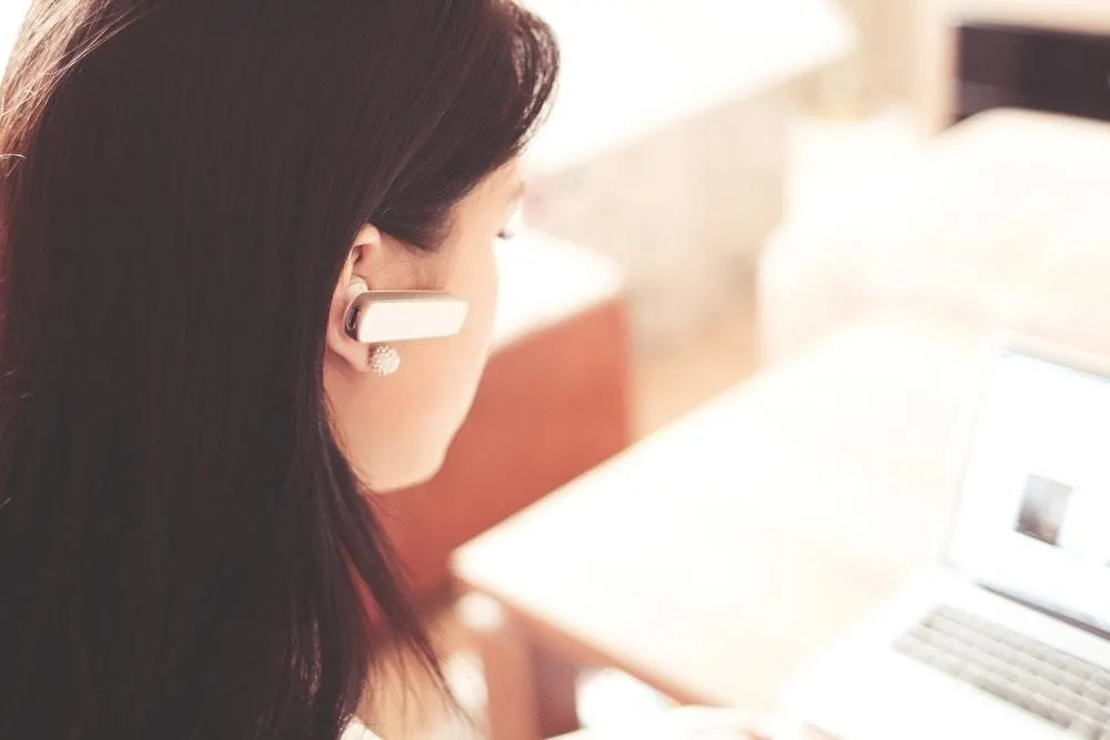 A woman wears an earpiece while sitting in front of a laptop.