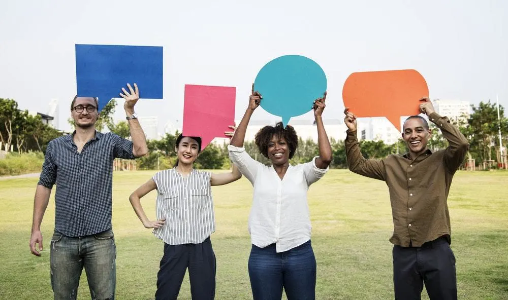 A diverse group of people stand smiling while holding speech bubbles in the air