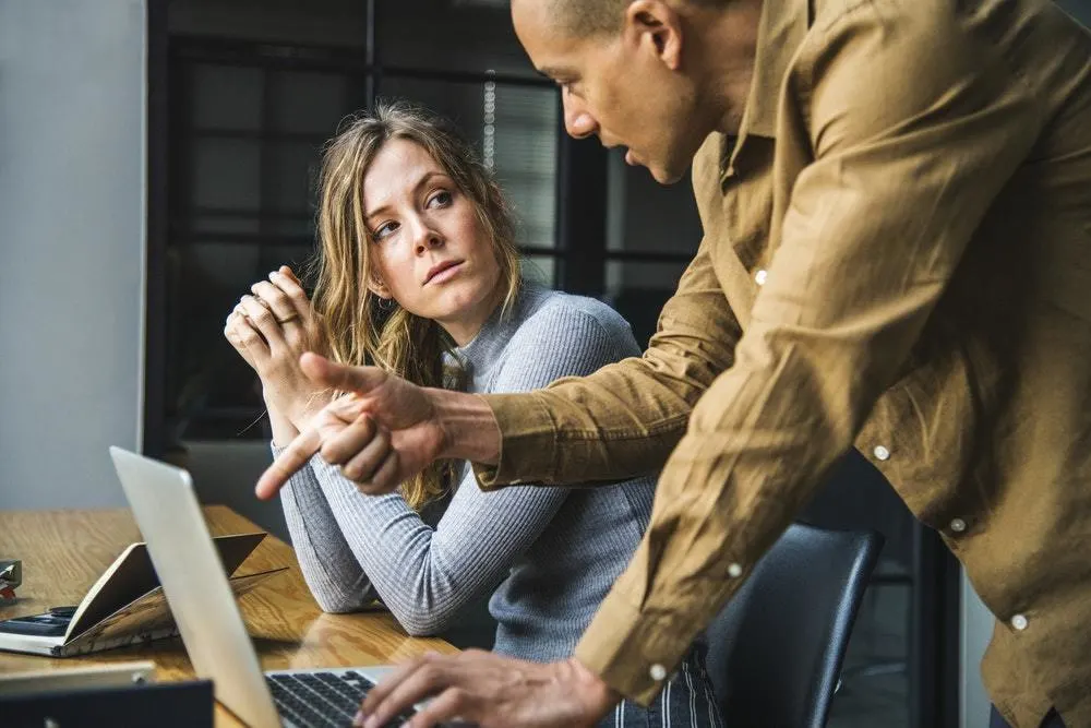 Man standing over a woman in an office setting.