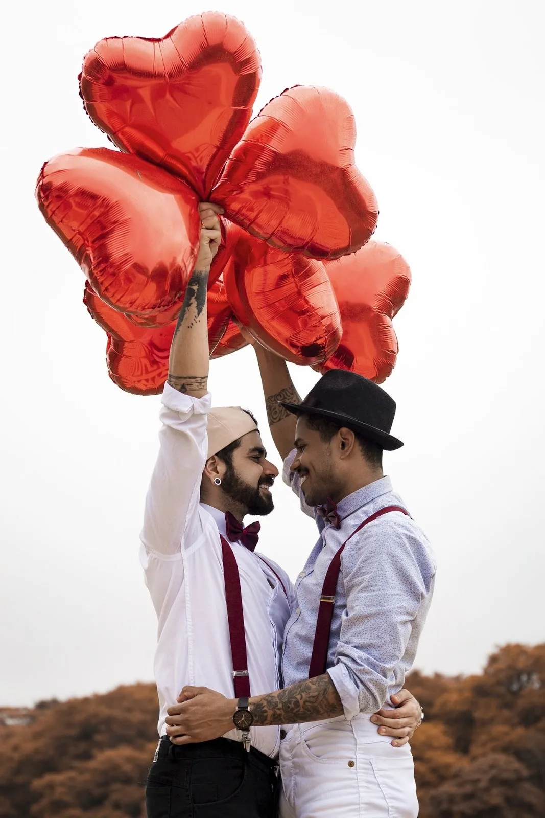 Photo d’un couple LGBTQ se regardant dans les yeux avec amour, tout en tenant des ballons en forme de cœur.