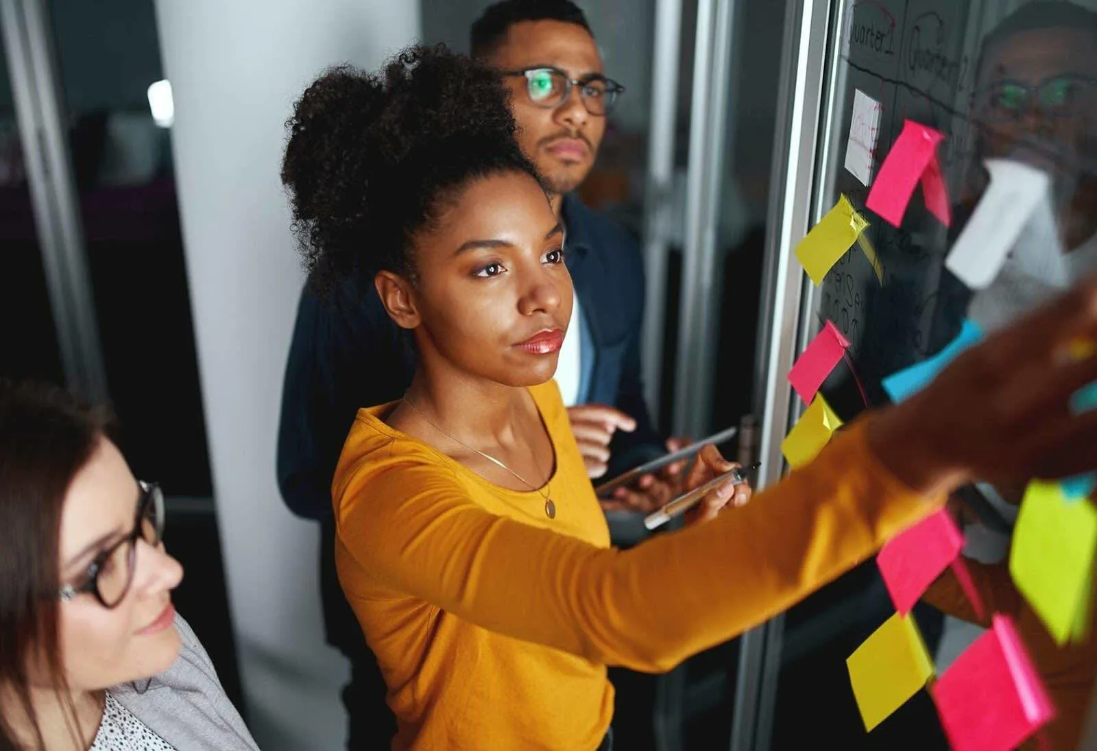 a person putting a sticky note on a wall with colleagues looking on