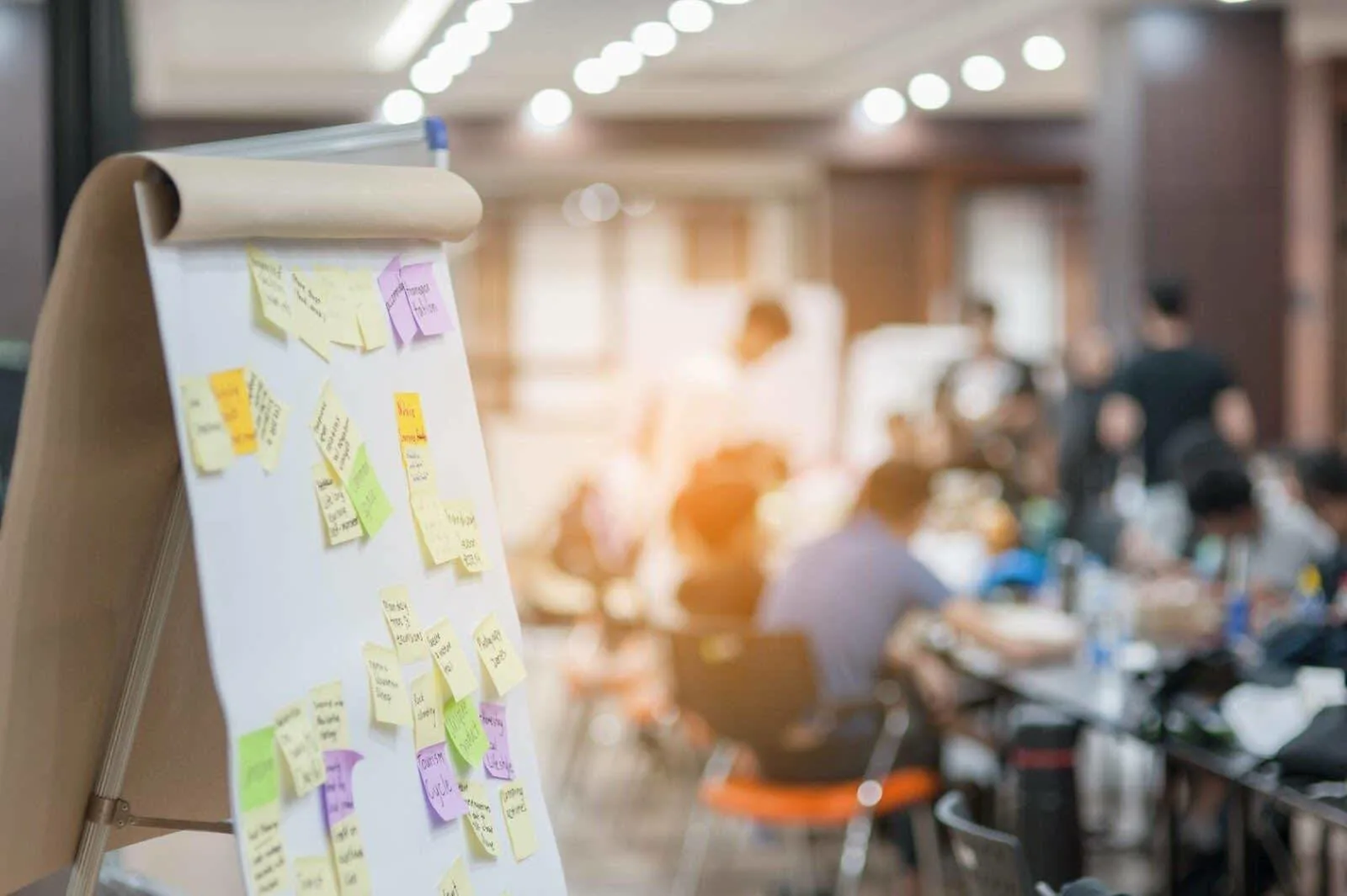 Photo où l’on peut voir des notes autocollantes sur un tableau et, en arrière-plan, des personnes qui travaillent