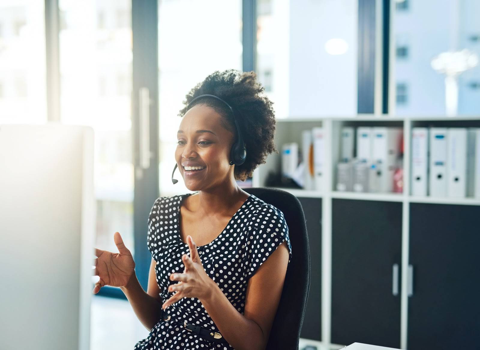 A smiling person talking on the phone with a headset in an office.