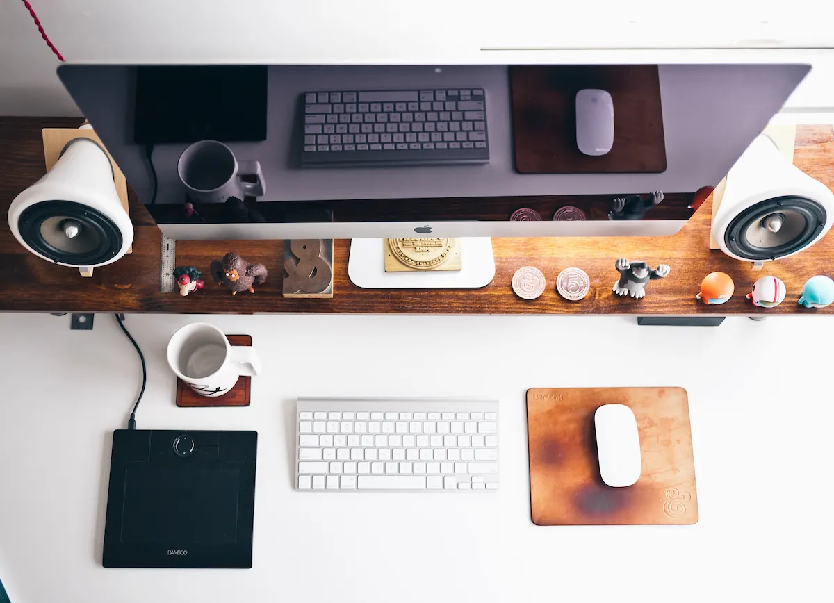 A Mac screen, keyboard, and mouse on a desk with knickknacks.