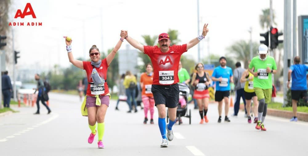 Two runners wearing Adim Adim shirts run down a road with their hands clasped above their heads in a victorious gesture.