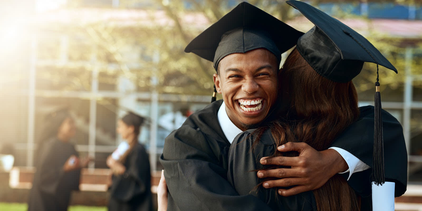 Young man wearing a graduation cap and gown hugging woman also wearing a cap and gown.