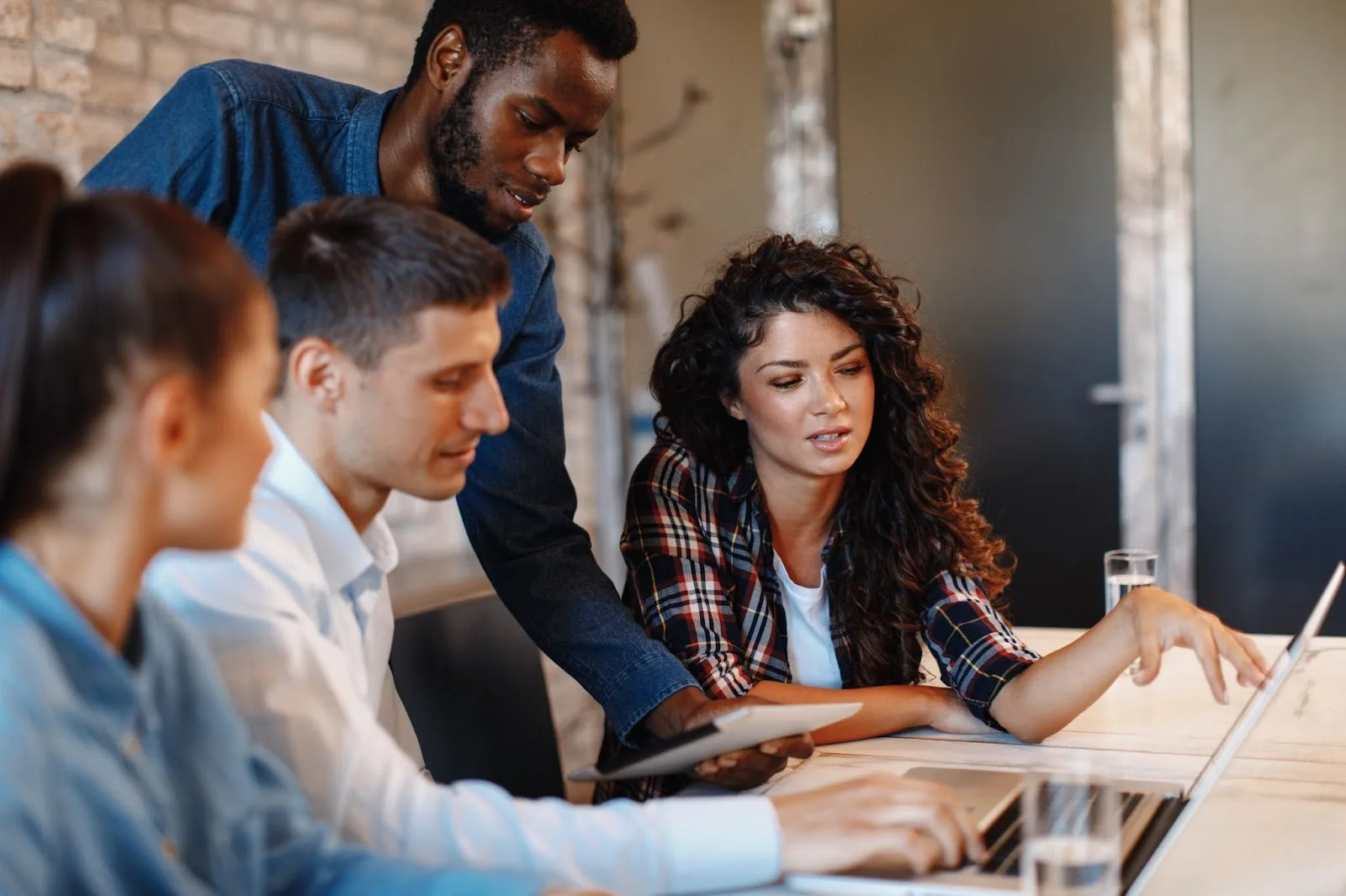 Four members of a quality team huddled around a laptop discussing a project.