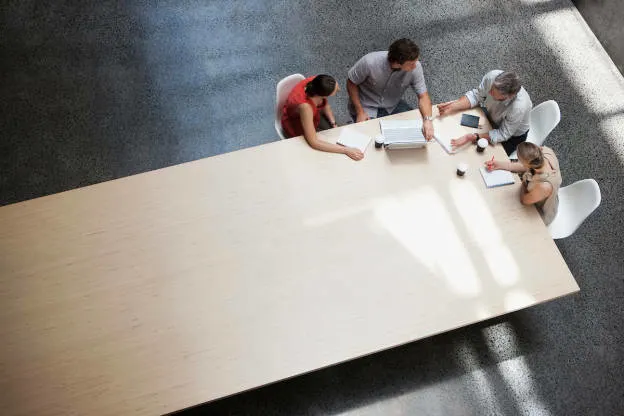 A sales operations professional getting input from leaders across the company at the corner of a long table.