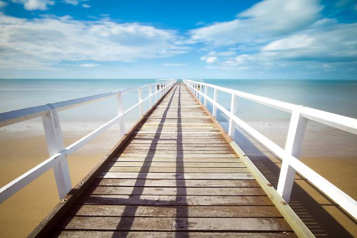 Empty bridge extending from the shoreline out to the ocean.