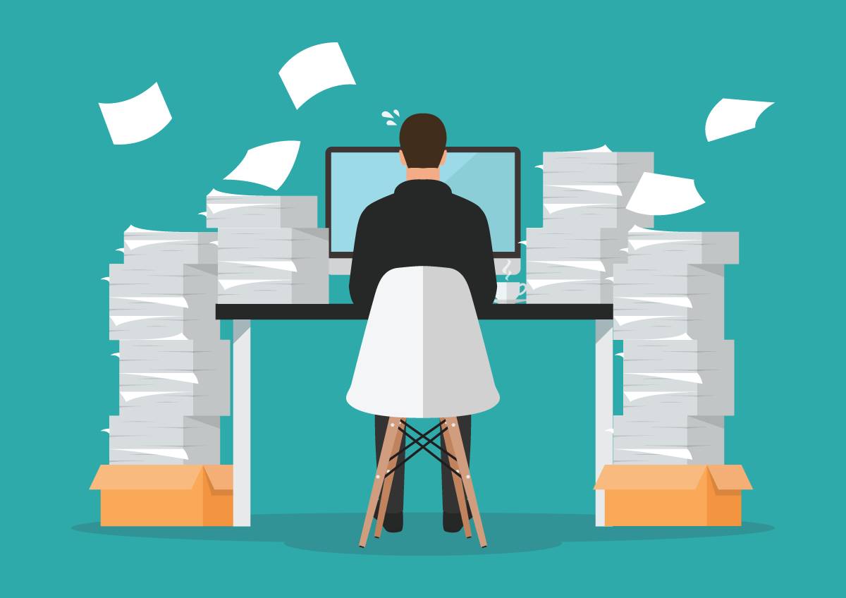 A person sitting in front of their laptop with tall stacks of paper on either side representing a daunting workload.