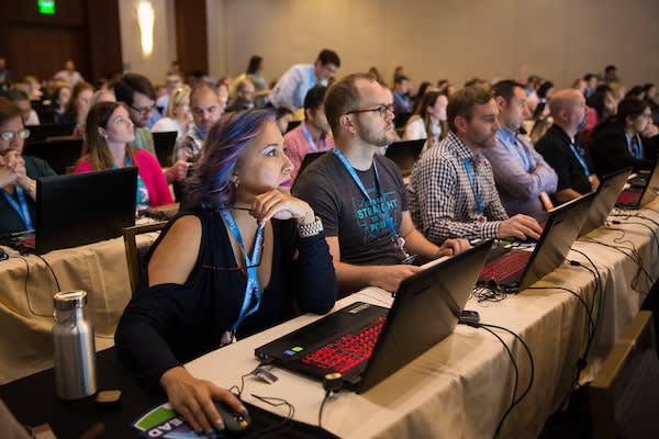 People in a conference room with laptops listening to an instructor.