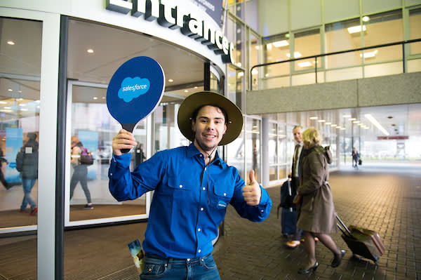 A volunteer with a sign welcoming people to an event.