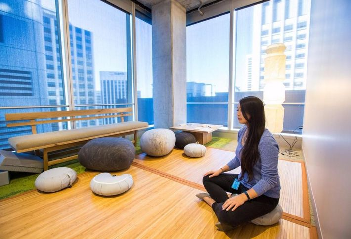 Image of a Salesforce meditation zone with a person sitting cross-legged on the hardwood floor meditating.