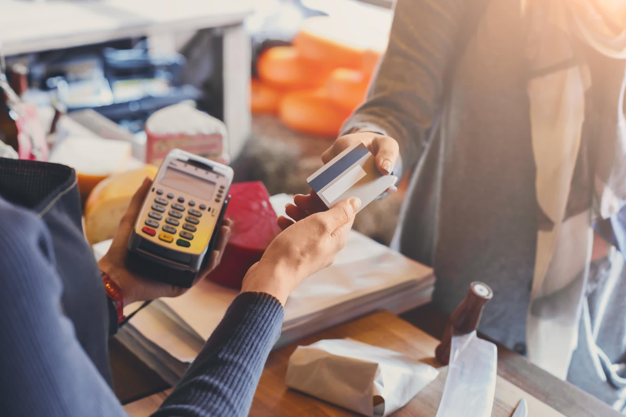 A shop keeper holding a credit card scanner, accepting a credit card from a customer