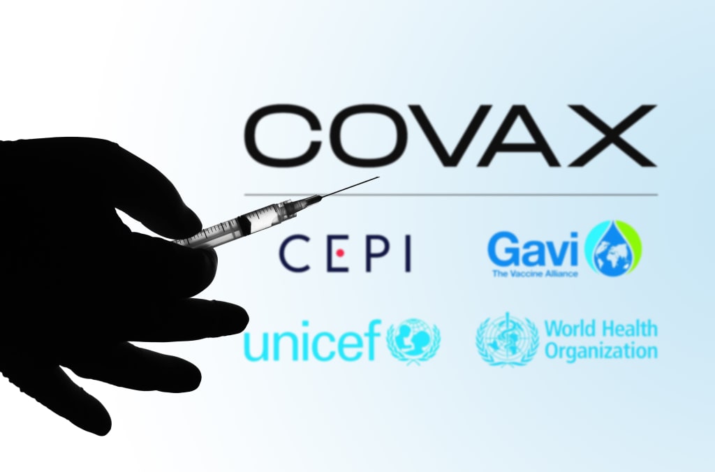 In this photo illustration the medical syringe is seen with COVAX Facility logo displayed on a screen in the background.
