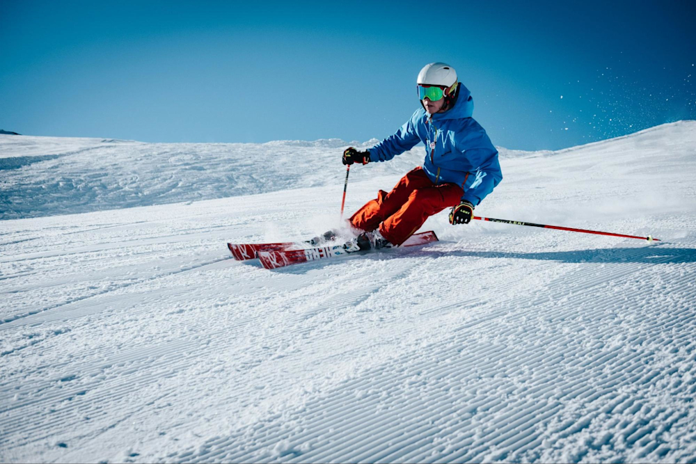 A skier who cross-trains with rowing goes down a snowy hill on skis.