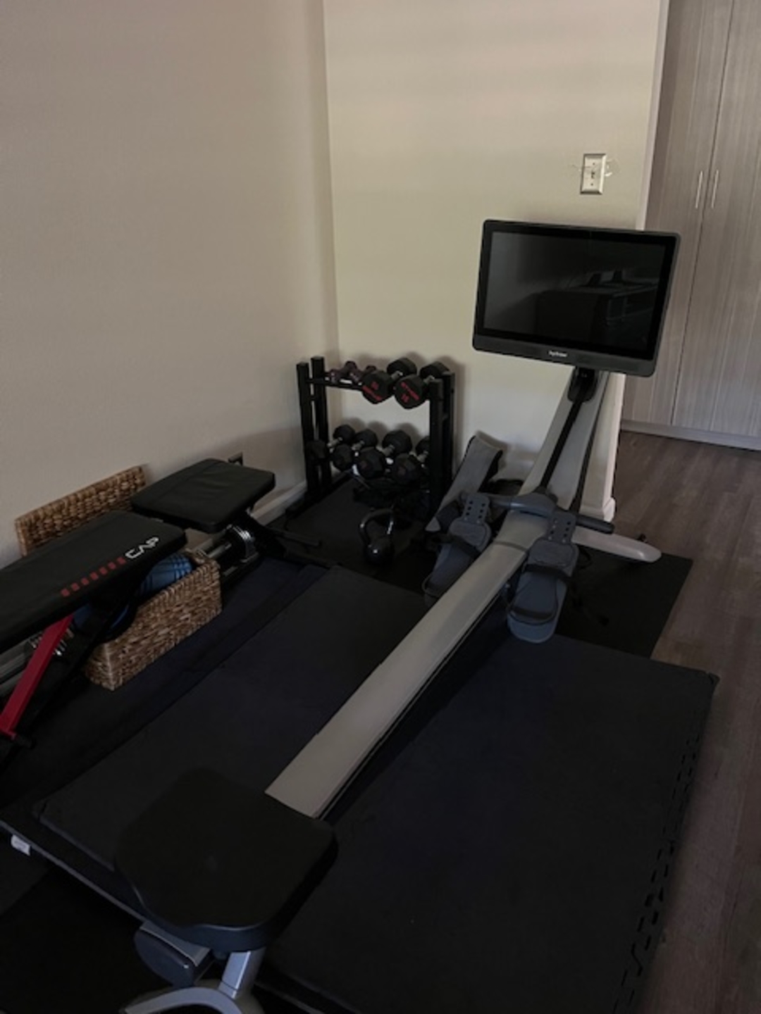An image of Hydrow member Keith's home gym setup, including weights and a Hydrow rowing machine.