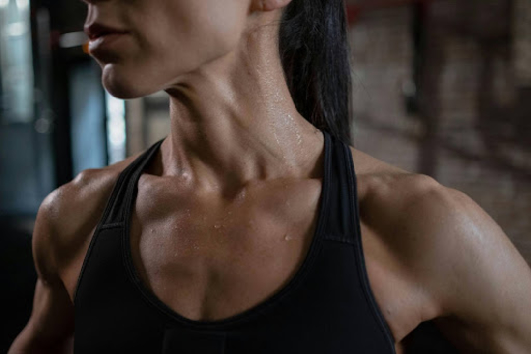 A sweating woman in a gym shows off her chest muscles.