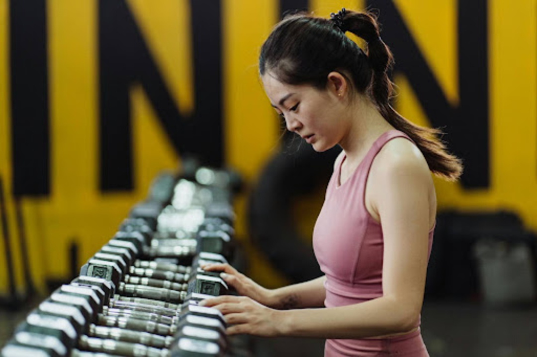 Woman selects a dumbbell weight at the gym after learning about the best dumbbell workouts for beginners.