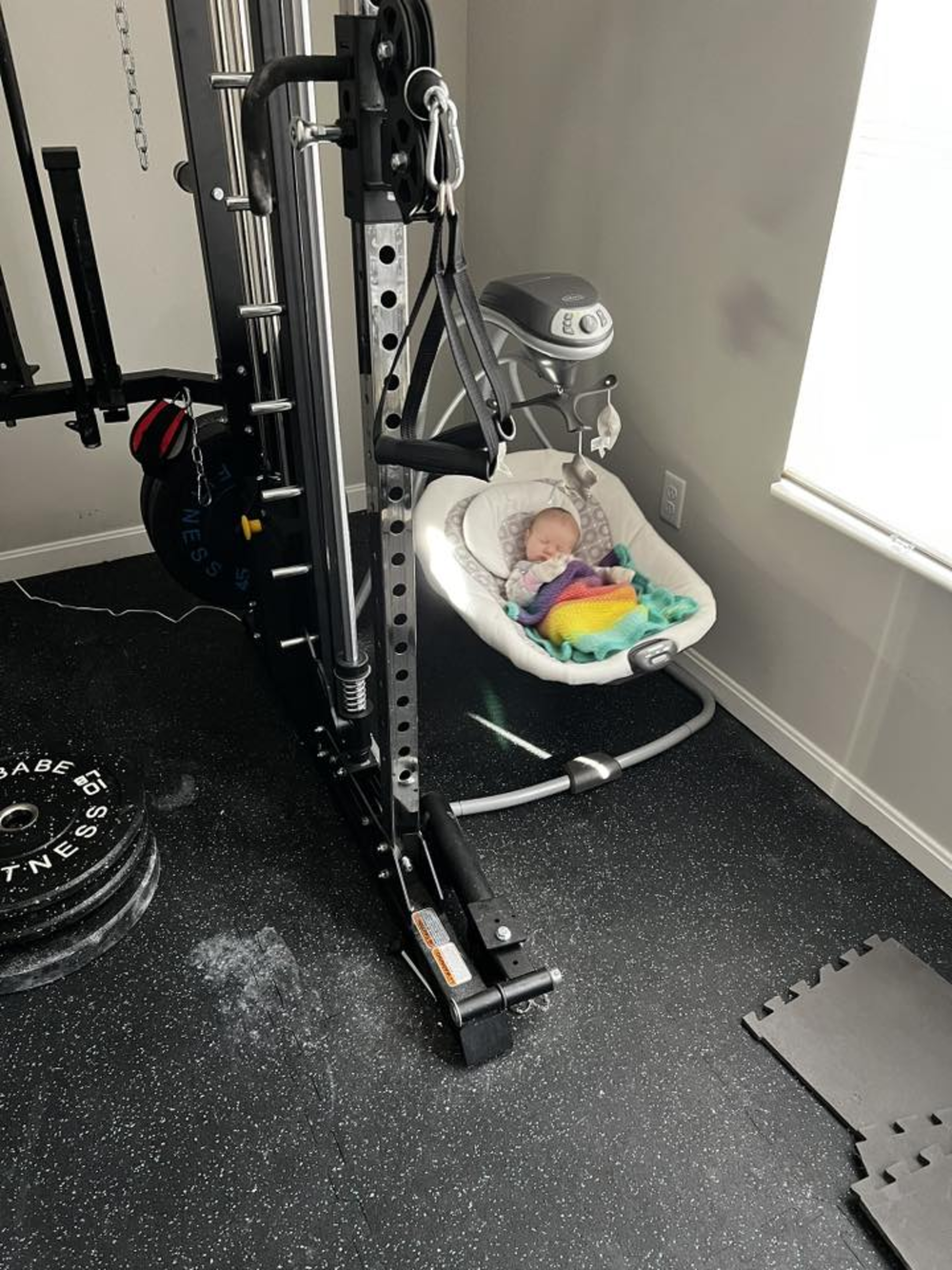 A baby sleeps in a rocker in a home gym.