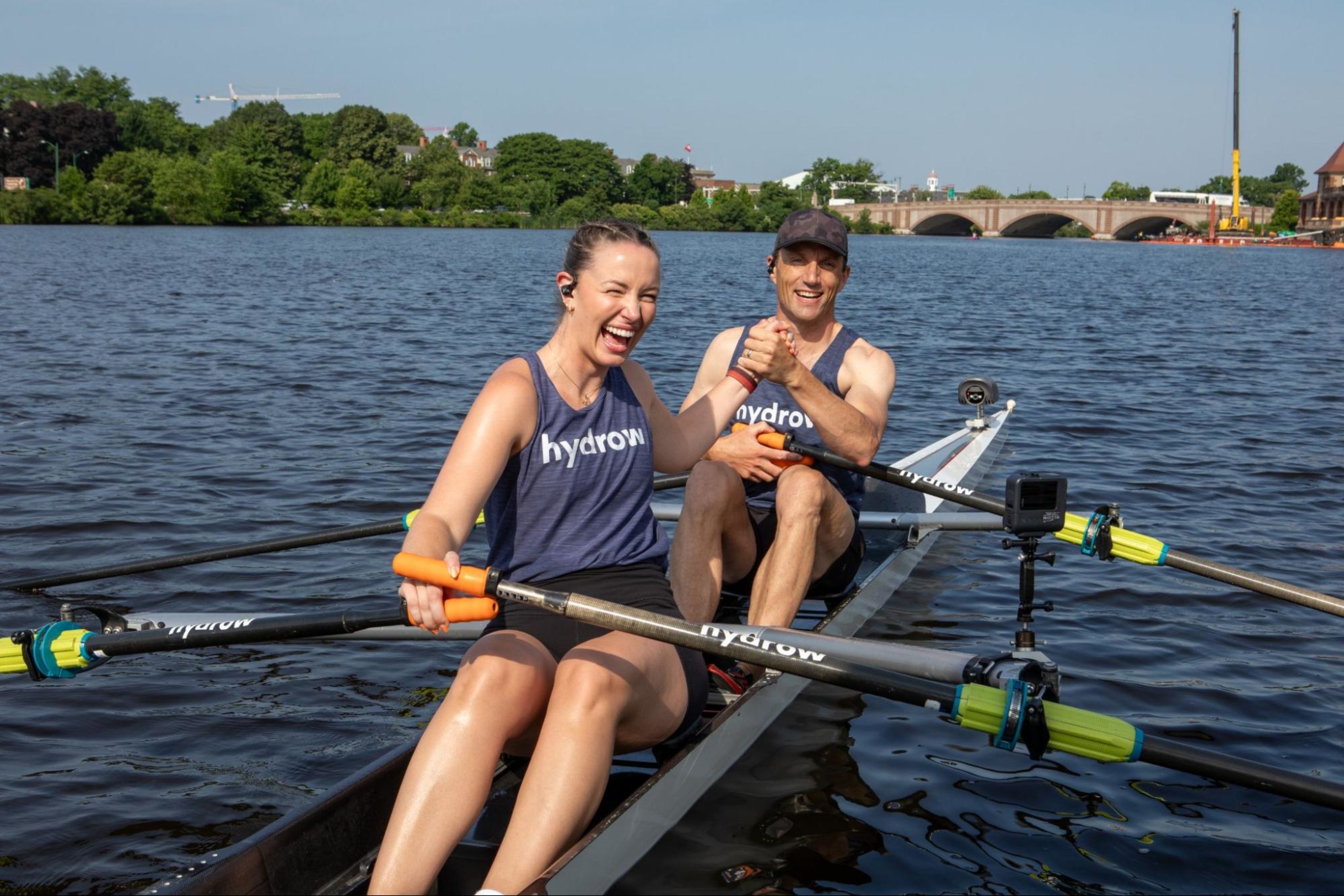 Hydrow Athletes high-five while doing a rowing workout on the water.