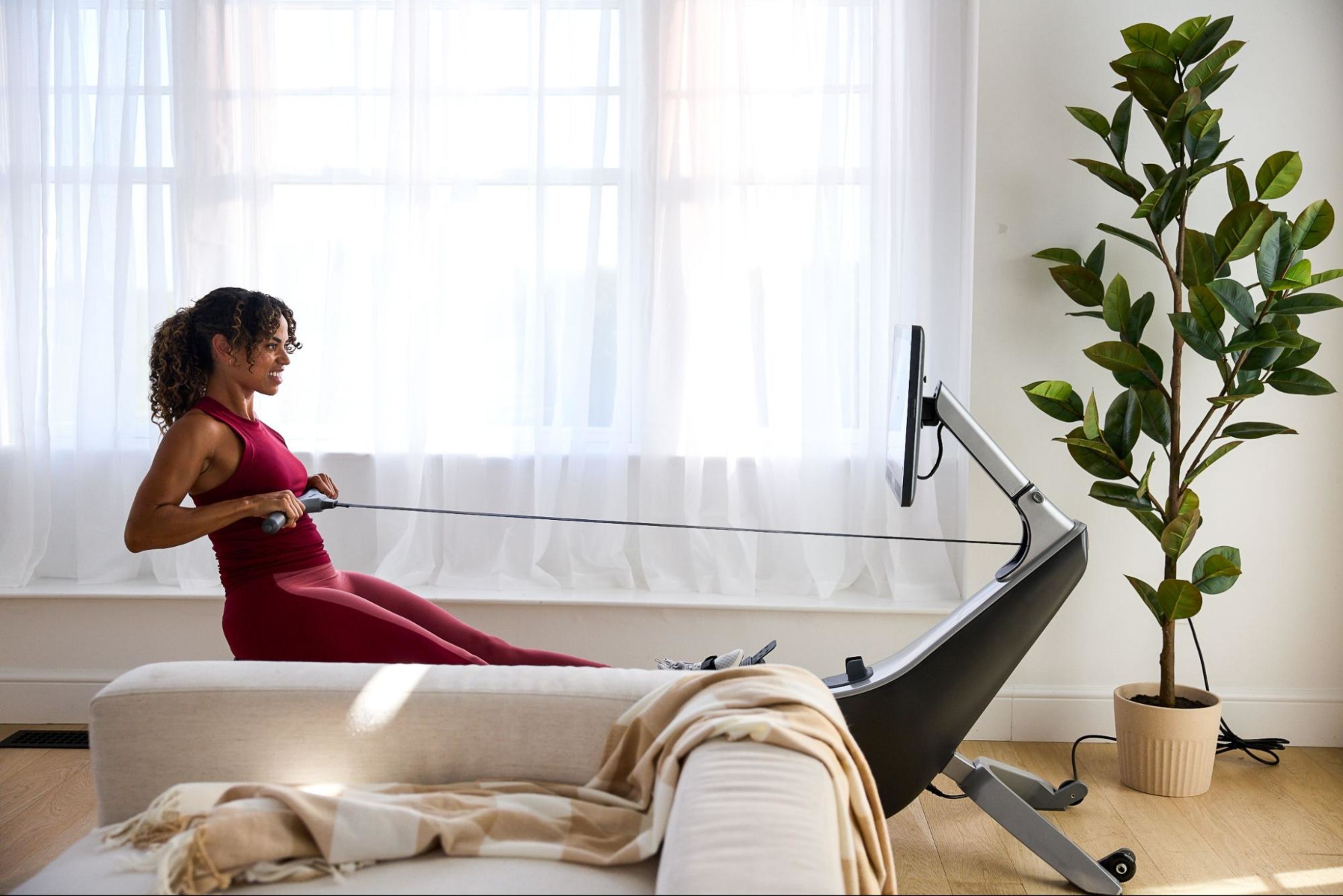 Woman rows in a rowing machine after figuring out how much space she needs to set up a rowing machine.
