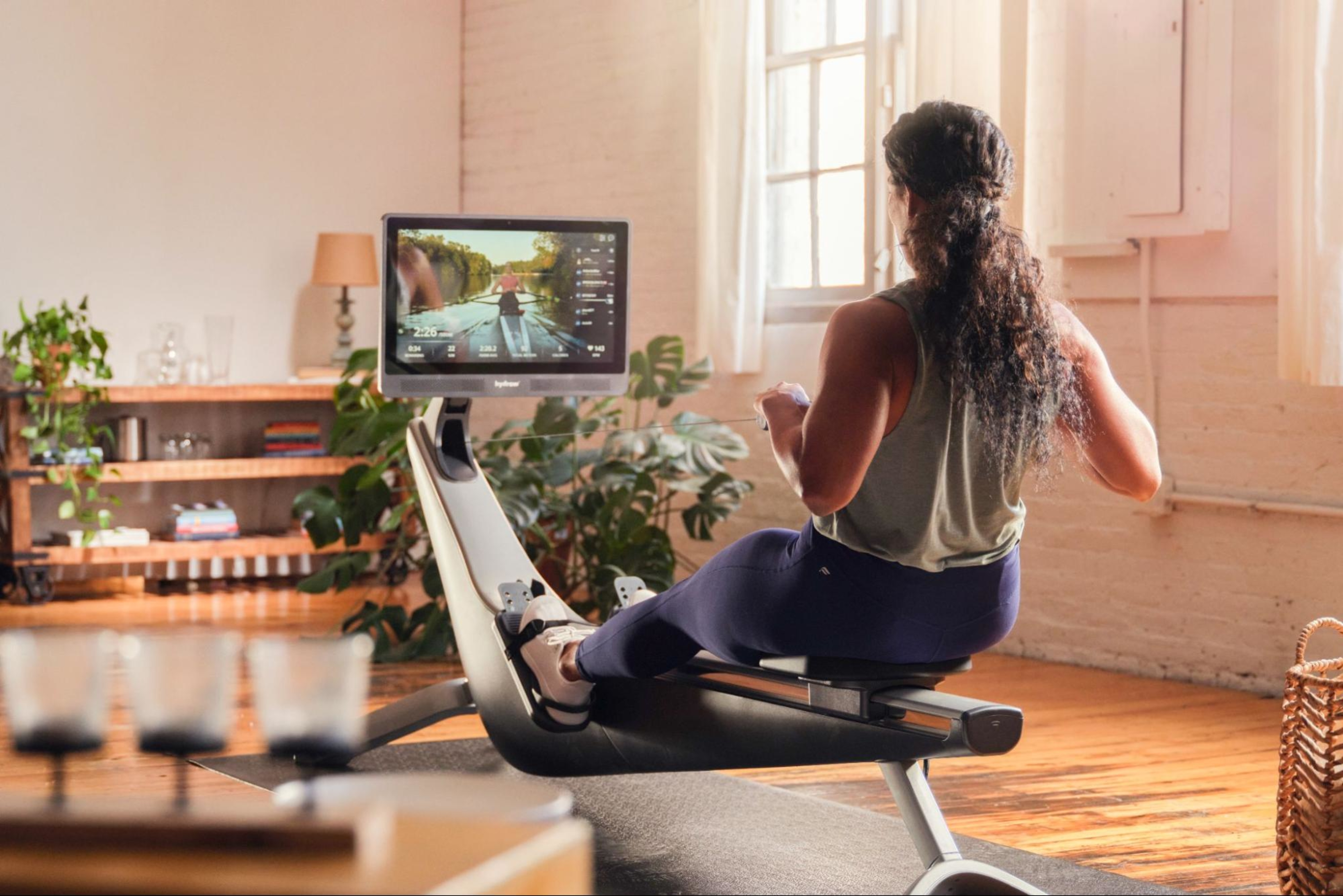 Woman works out on her rowing machine on top of a mat.