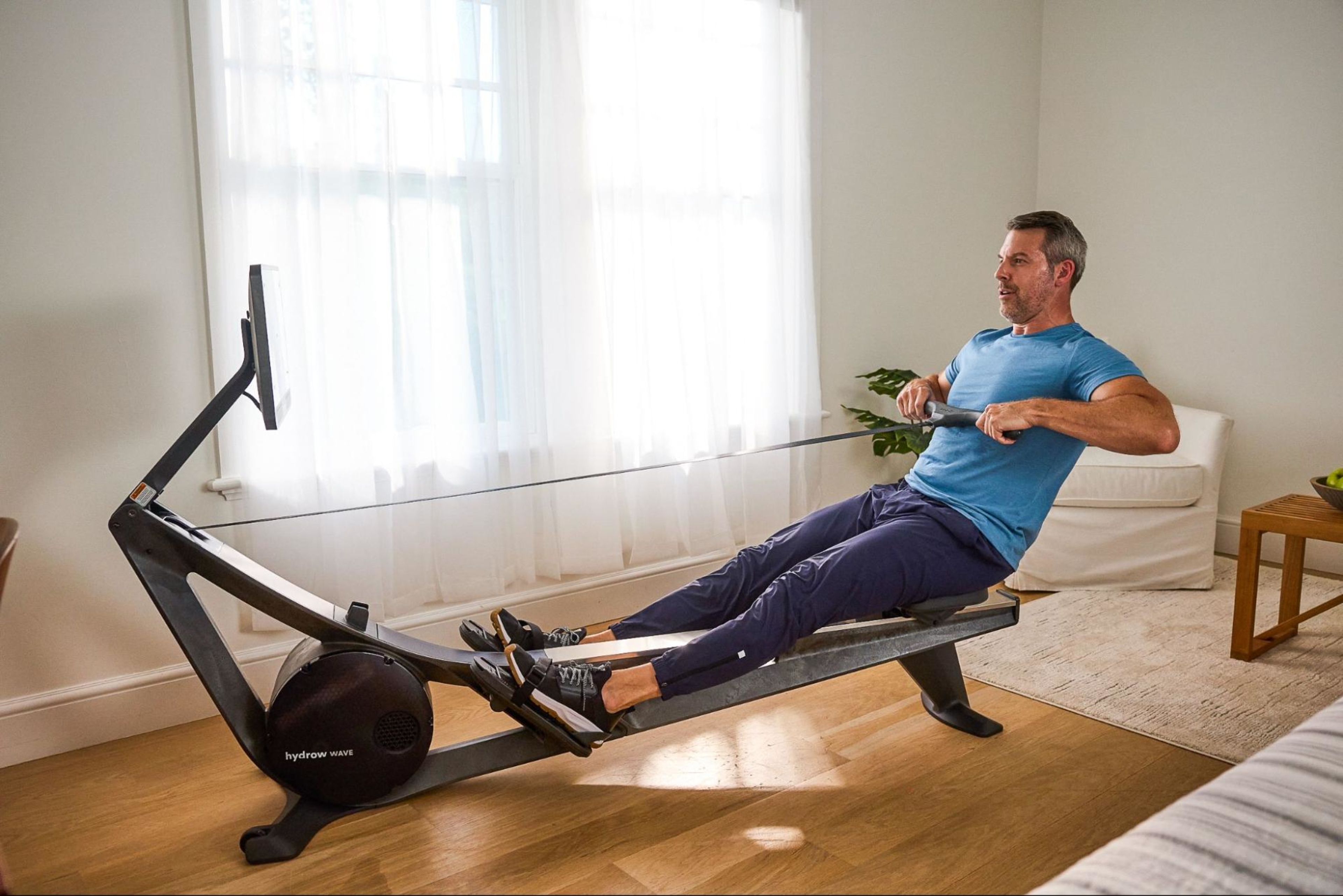 Busy professional man does a rowing machine workout at home.
