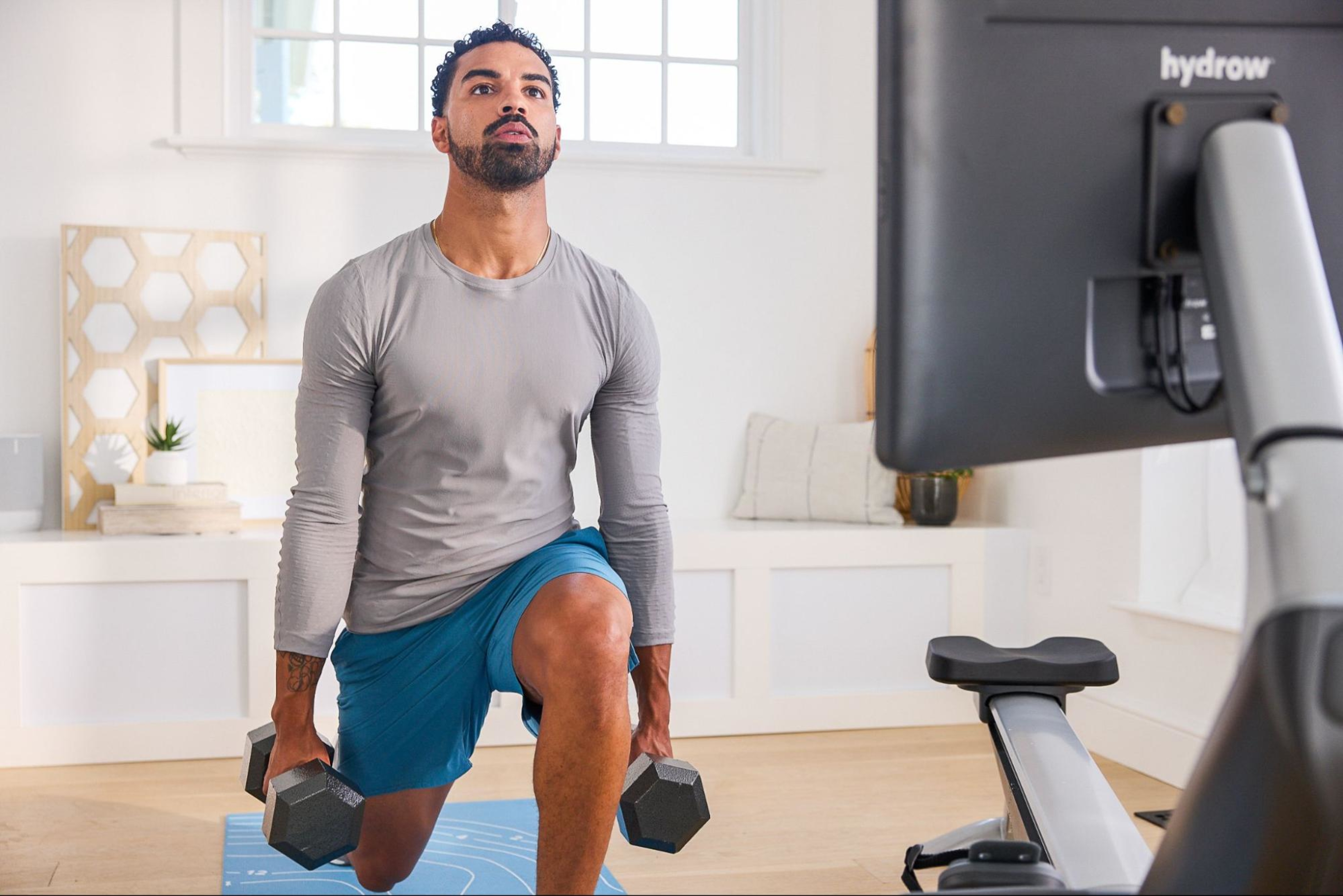 Man does an at-home workout for professionals with two heavy weights in front of a rowing machine.
