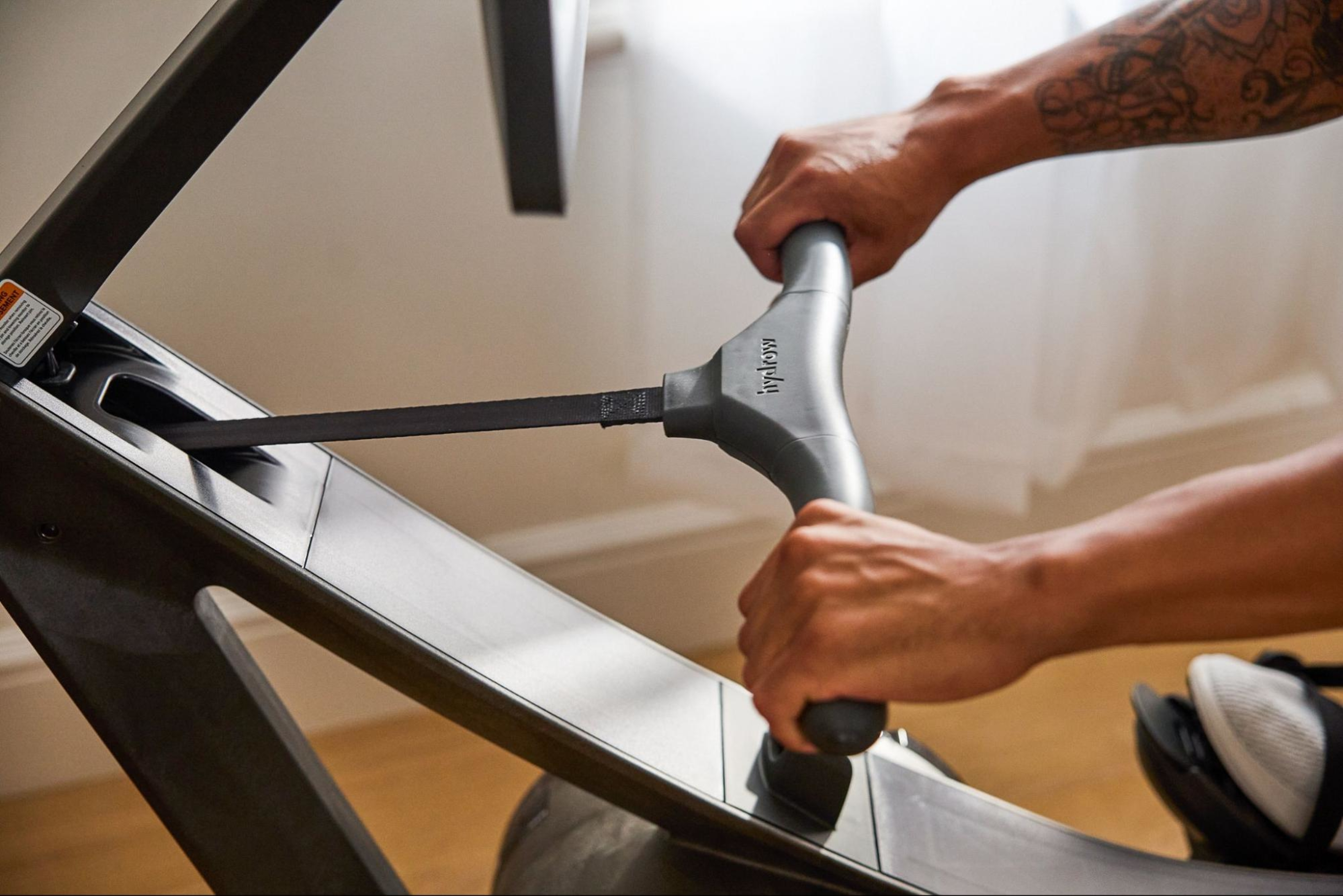 Man works out on a Hydrow rowing machine by pulling the handle.