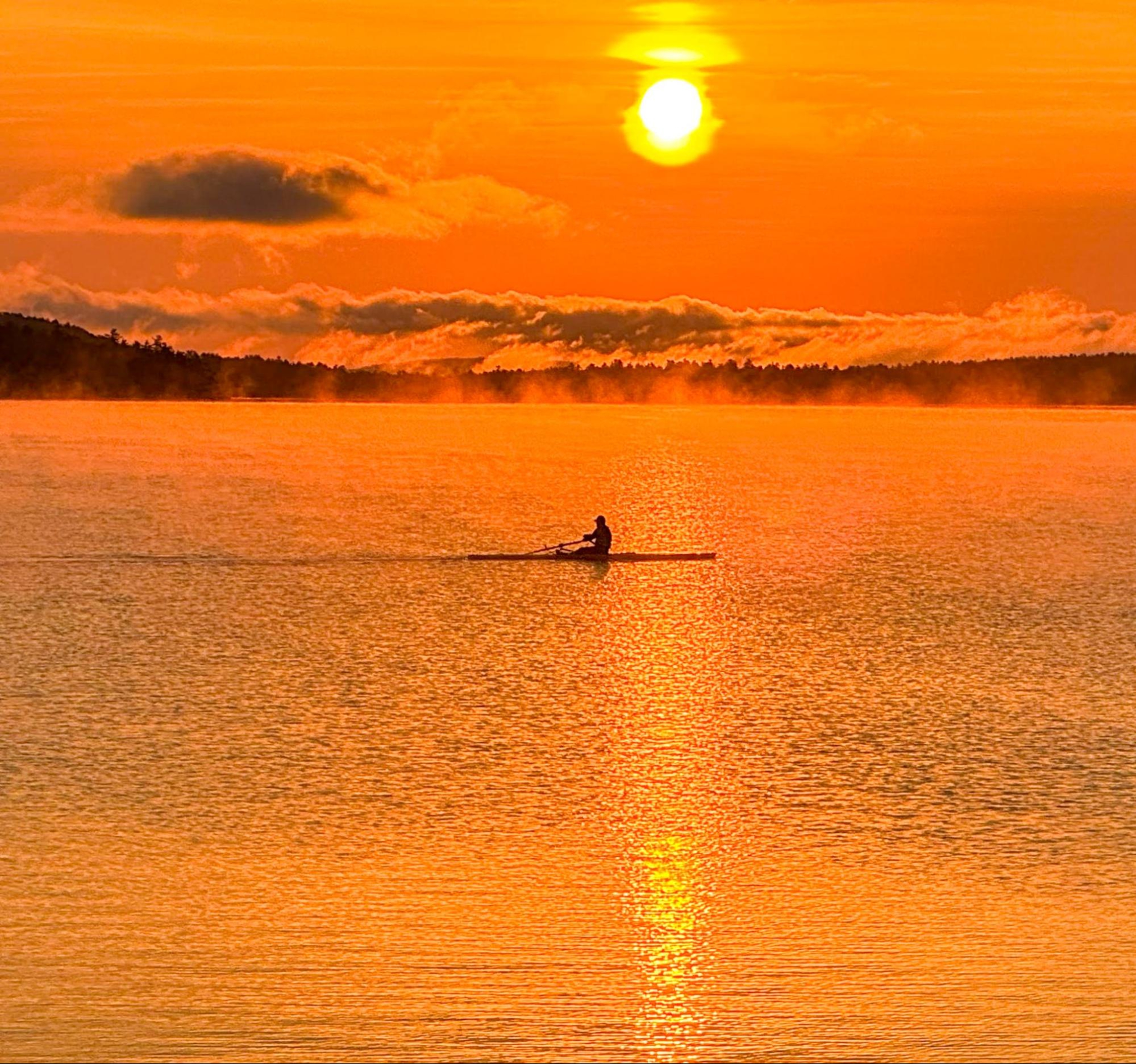 Hydrow member Bob Manley rows outdoors on a lake at sunset