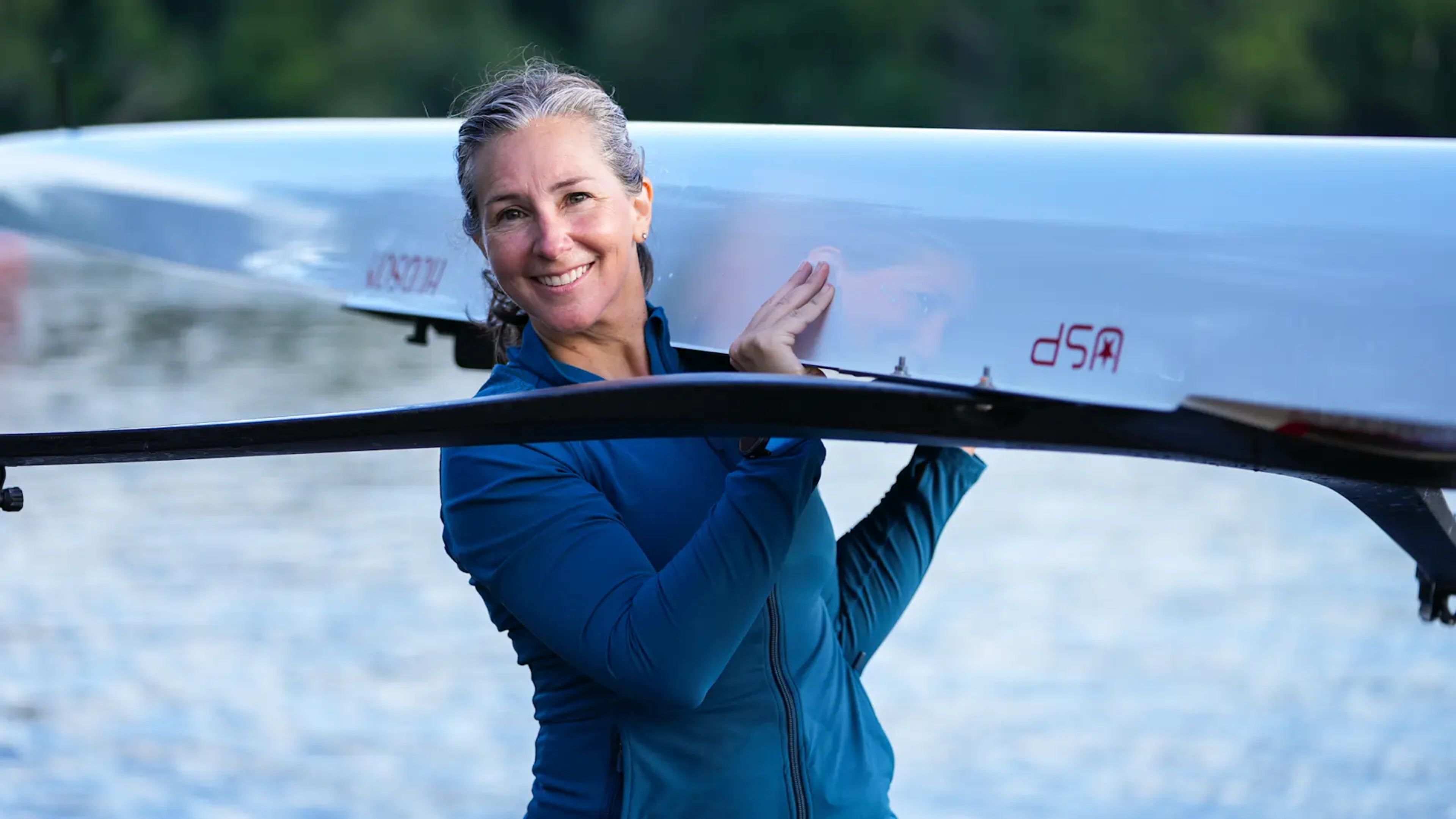 Megan Hanewald, Hydrow's lead personal coach, carries a scull over her shoulder.