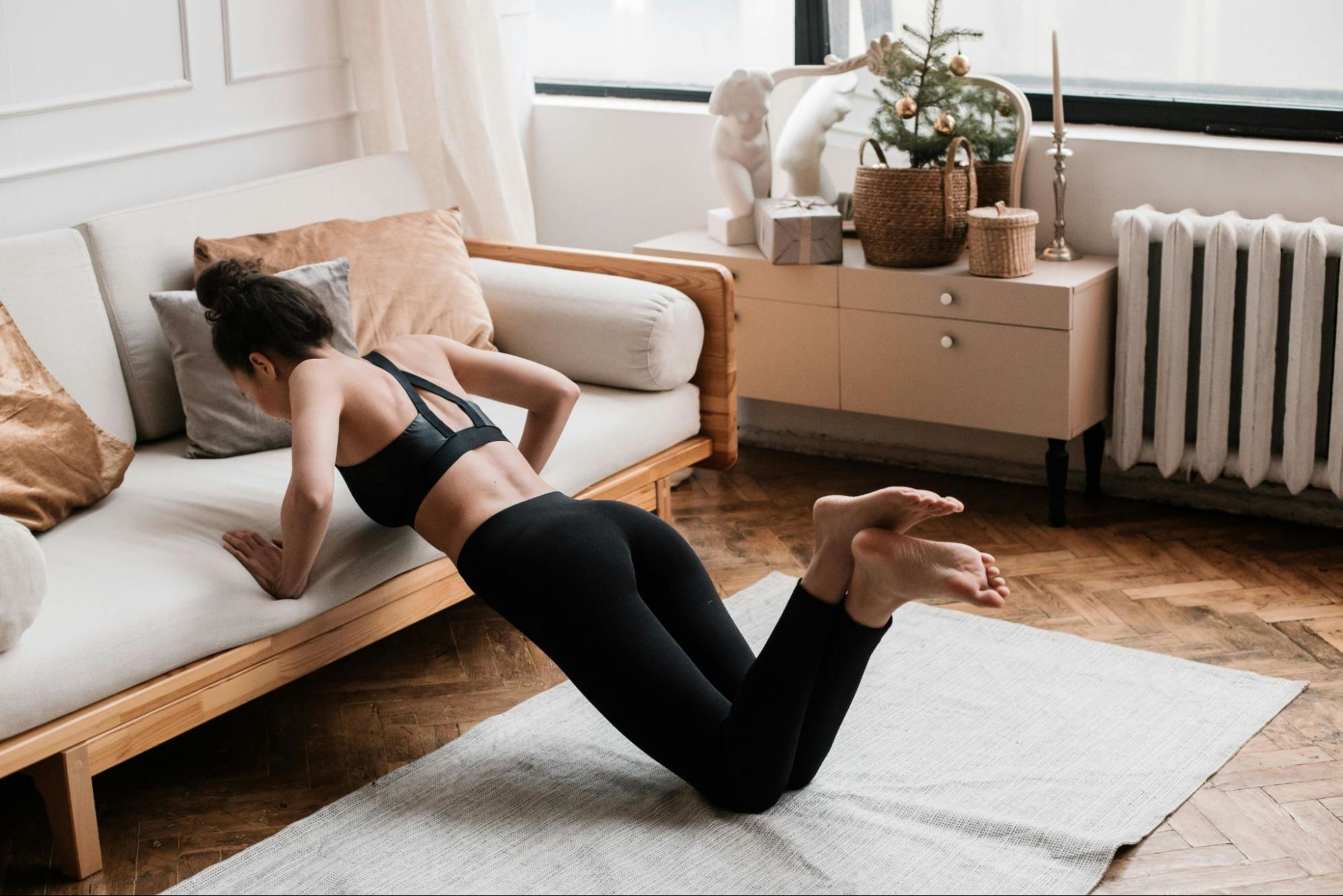 Woman does home muscle-building exercises by doing push-ups on her couch in her living room.