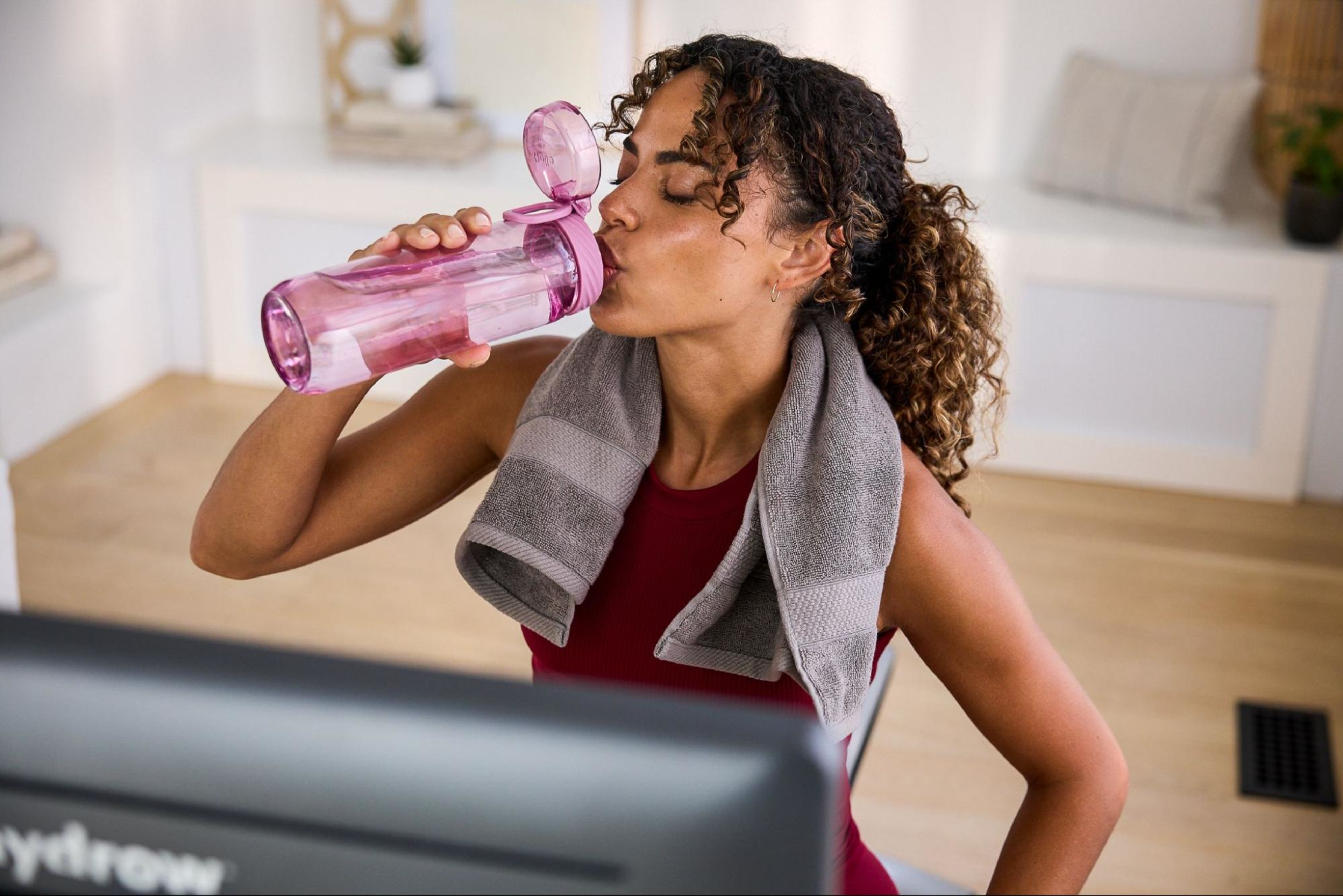 Woman drinks water after doing a cardio workout on her rowing machine.