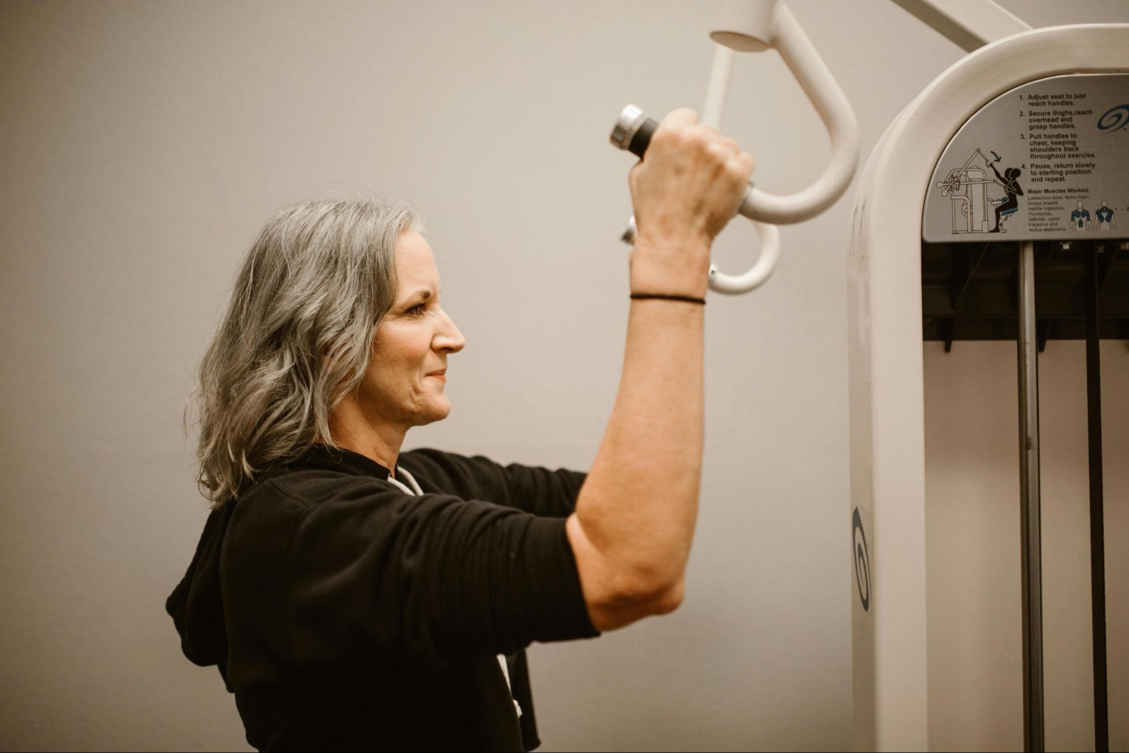 Woman works out on a machine at a gym doing the best strength training exercises for women after 50.