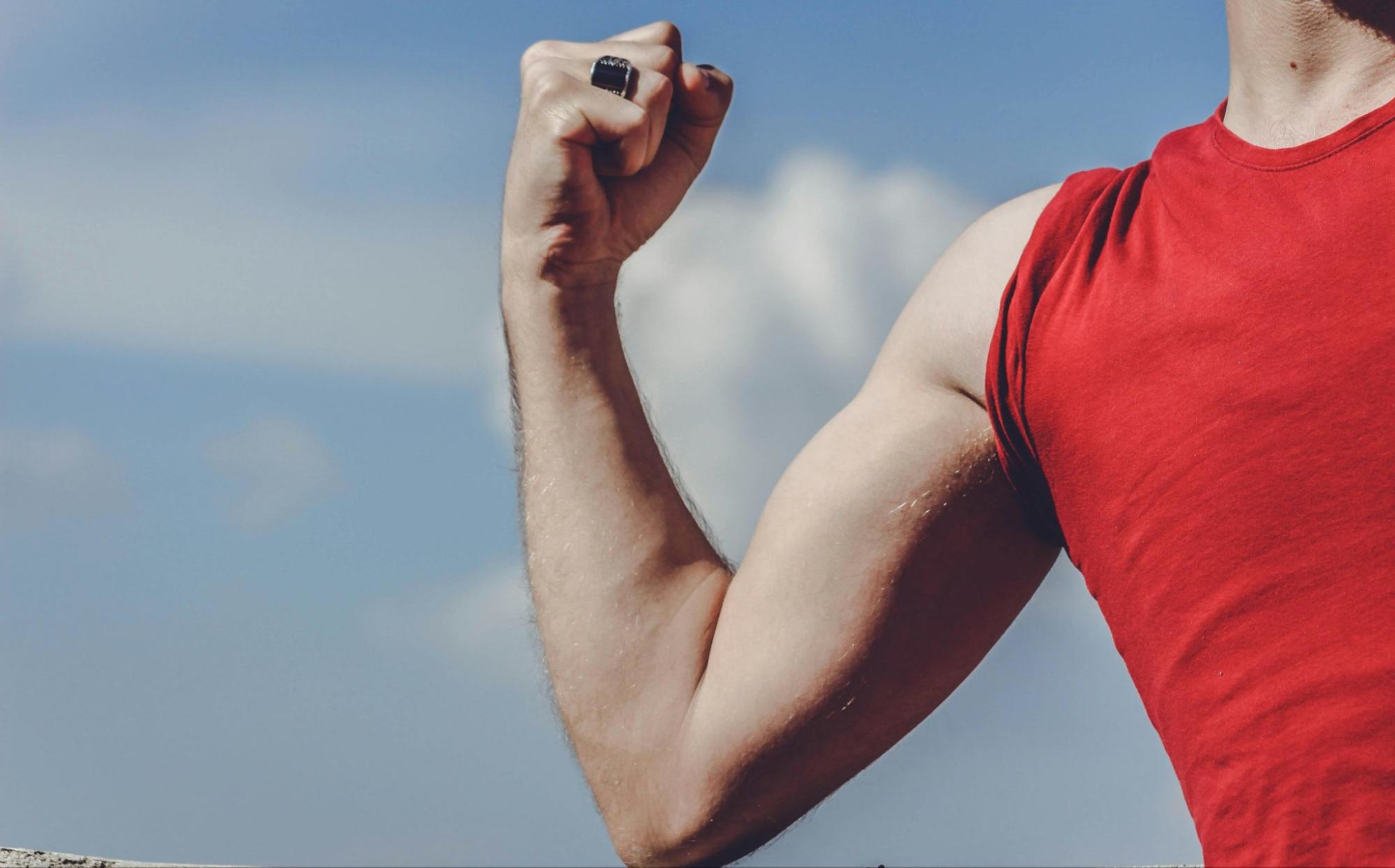 Man flexes arm muscle outdoors.