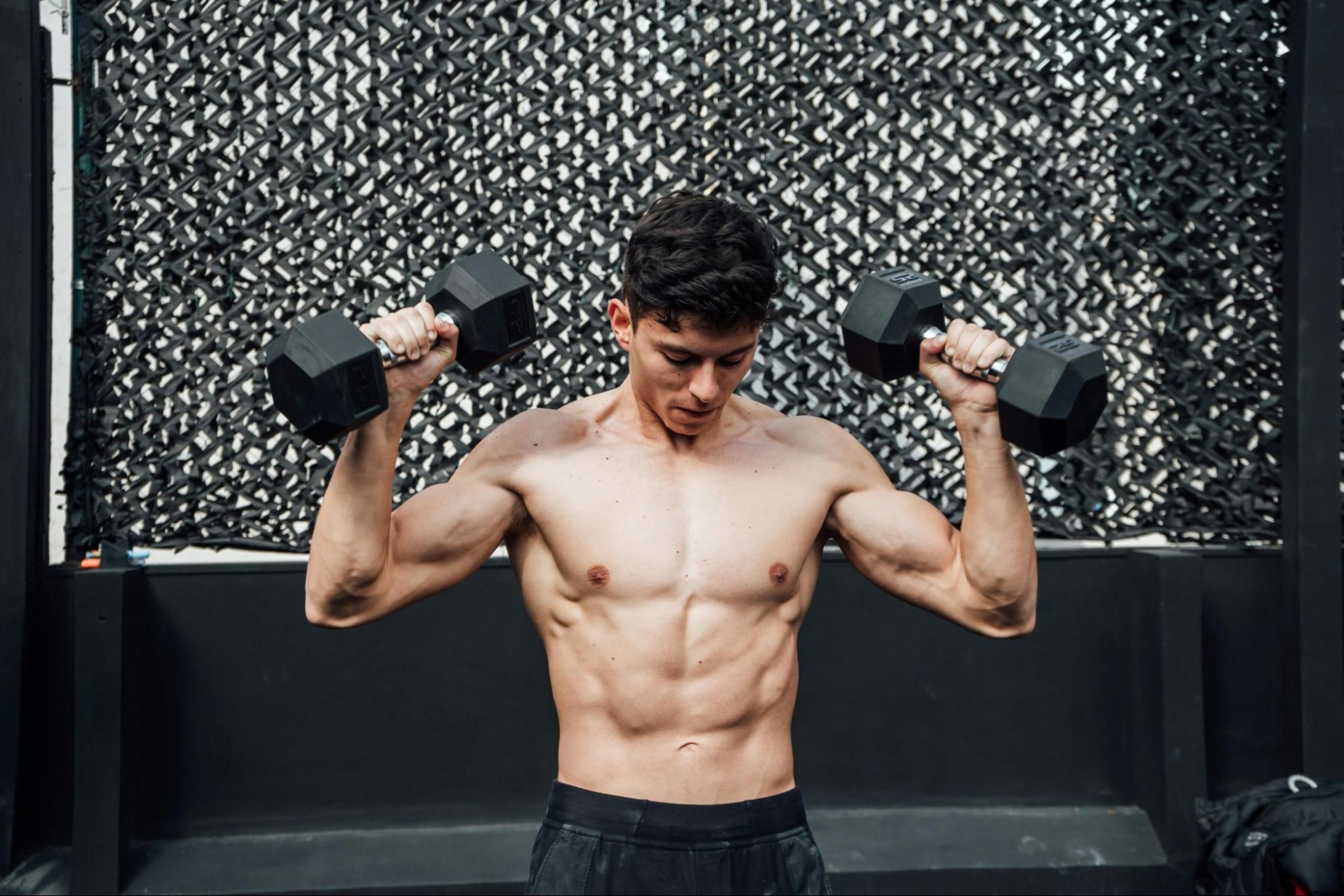 Man learns when to exhale during weight training while lifting two dumbbells shirtless.