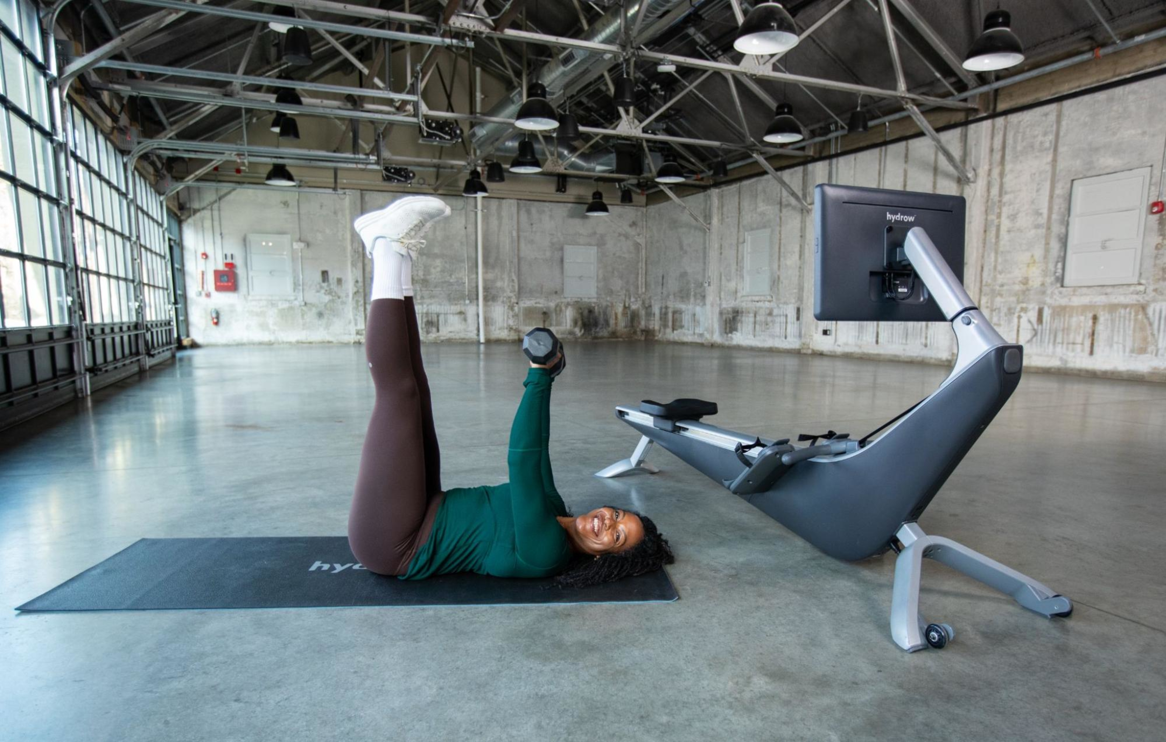 Hydrow Athlete demonstrates how to breathe when weight training while laying on the ground with a dumbbell.