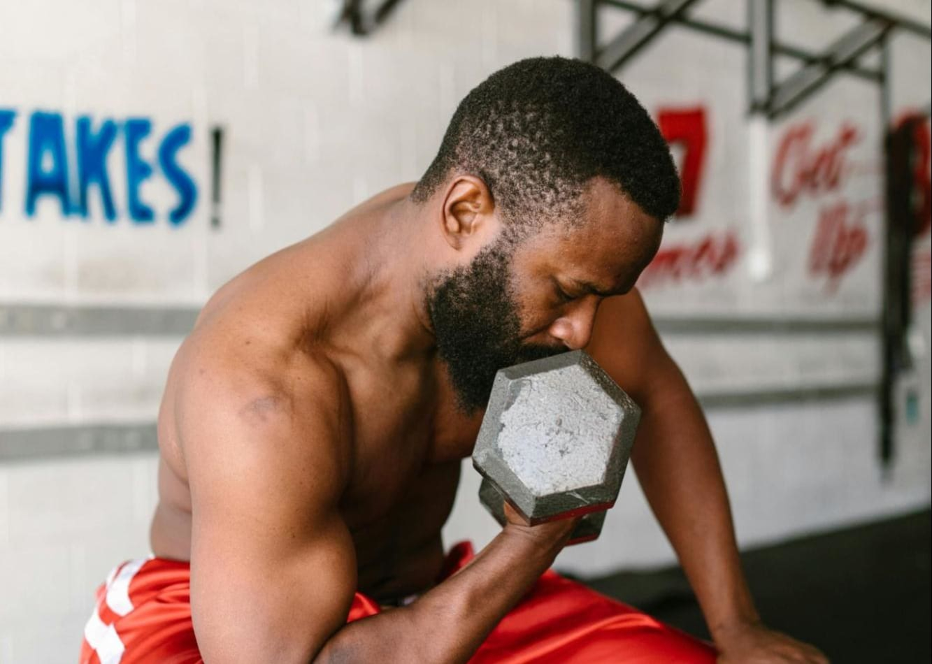 Man uses weight training breathing techniques while lifting a heavy dumbbell in a gym.
