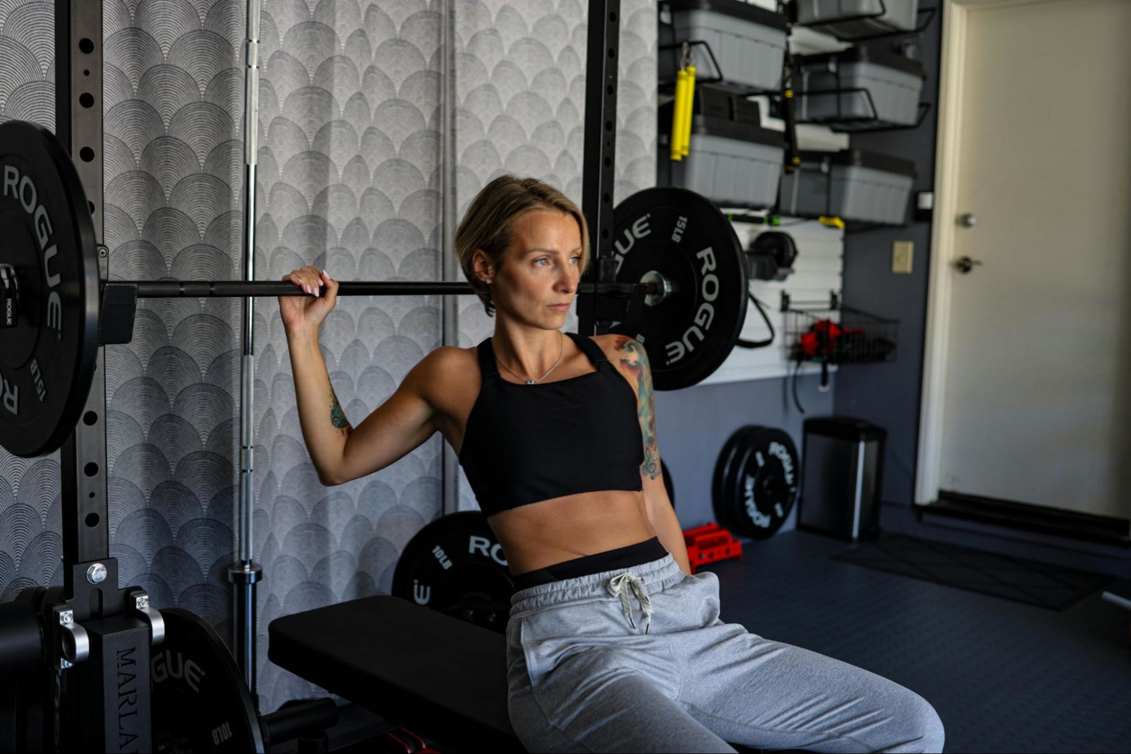 Woman sits in a home gym with a barbell and learns how often she should increase her weight with strength training.