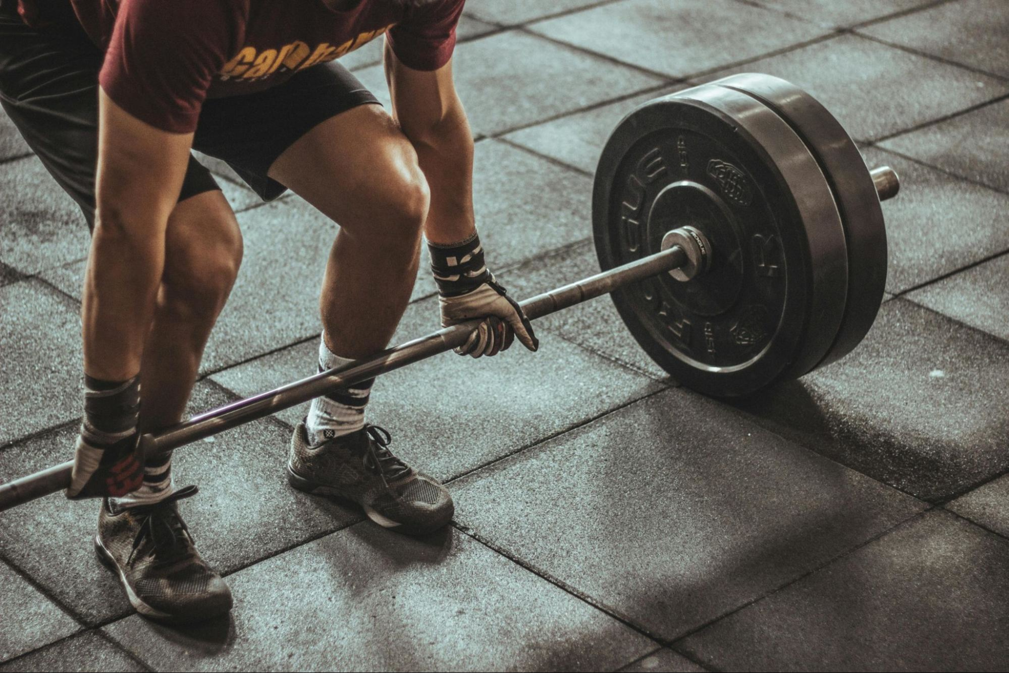 Man crouches to lift a barbell after learning how often to increase your weight when lifting.