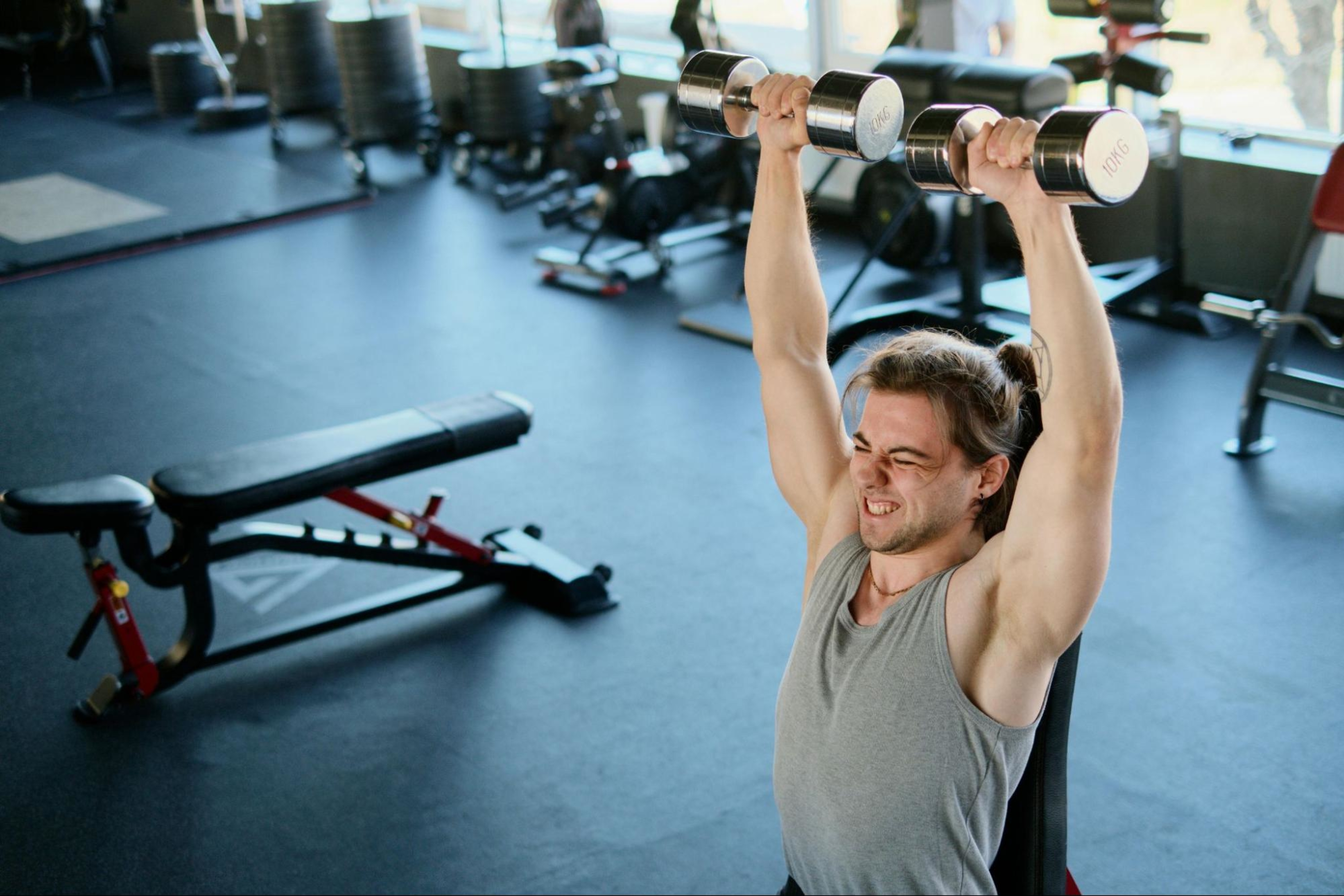 Man grimaces and lifts weights after learning when to increase weight when lifting.