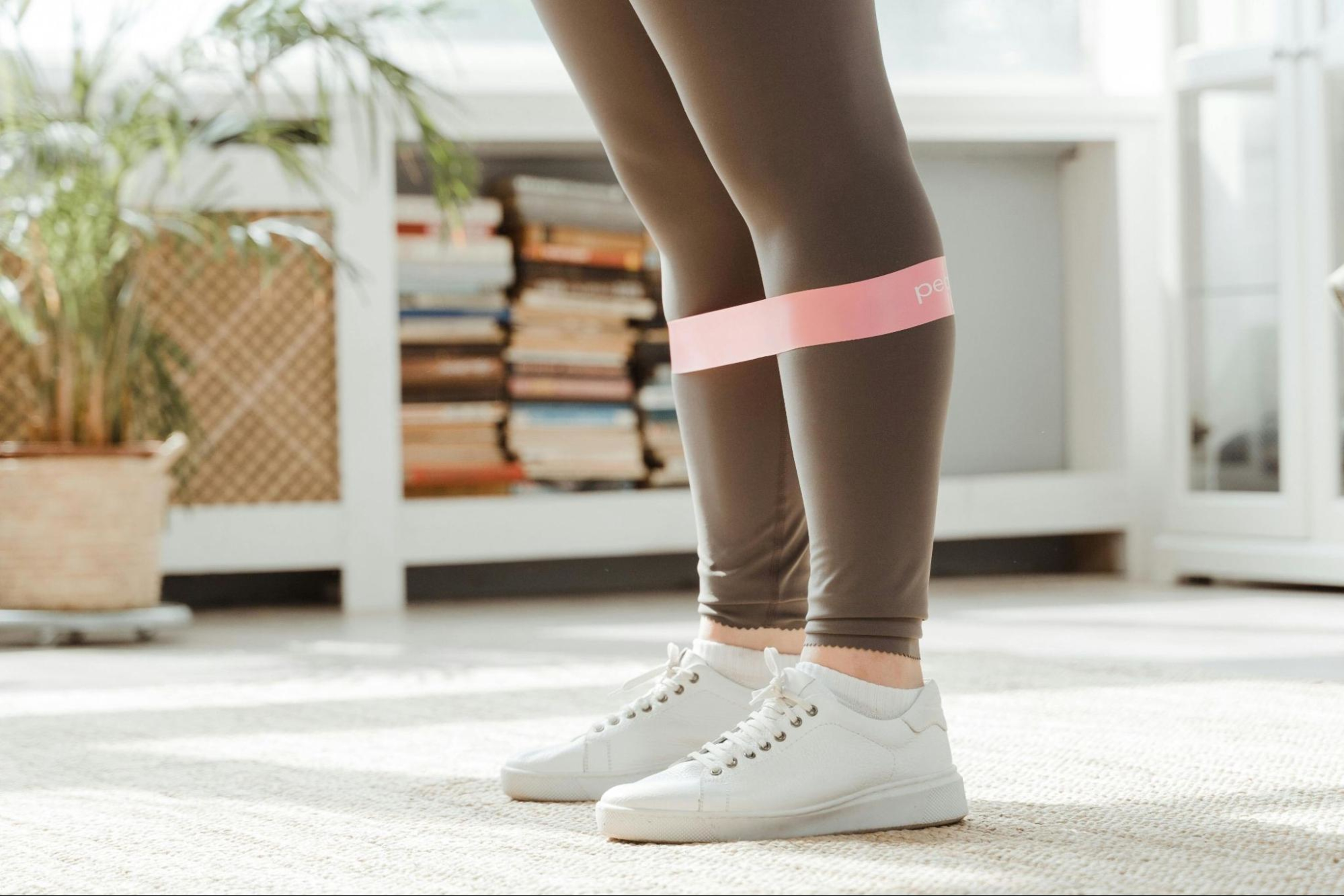 A woman prepares to do a leg routine for beginners with a pink resistance band around her legs.