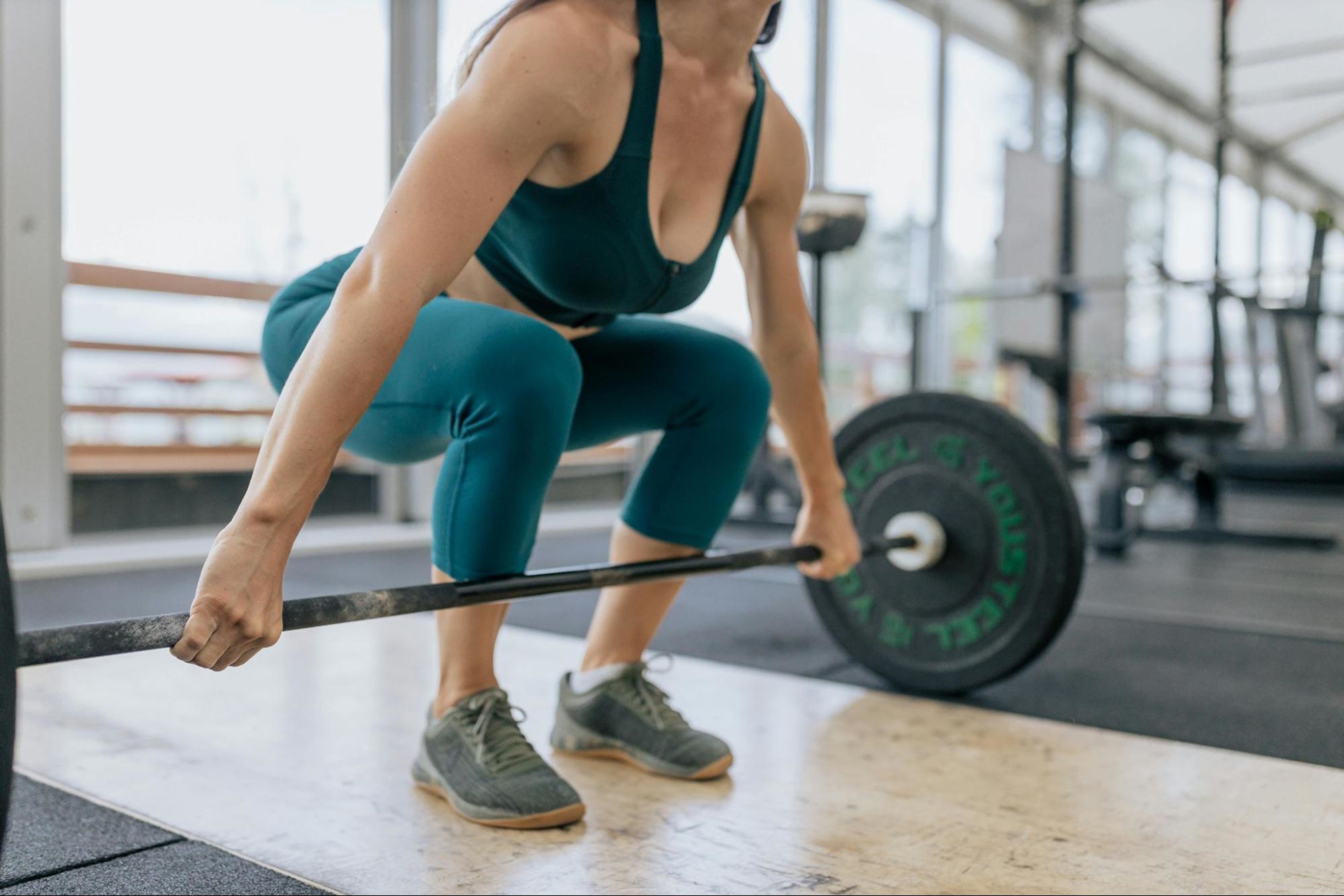Woman deciding between split training vs. a full-body workout lifts a barbell in a gym.