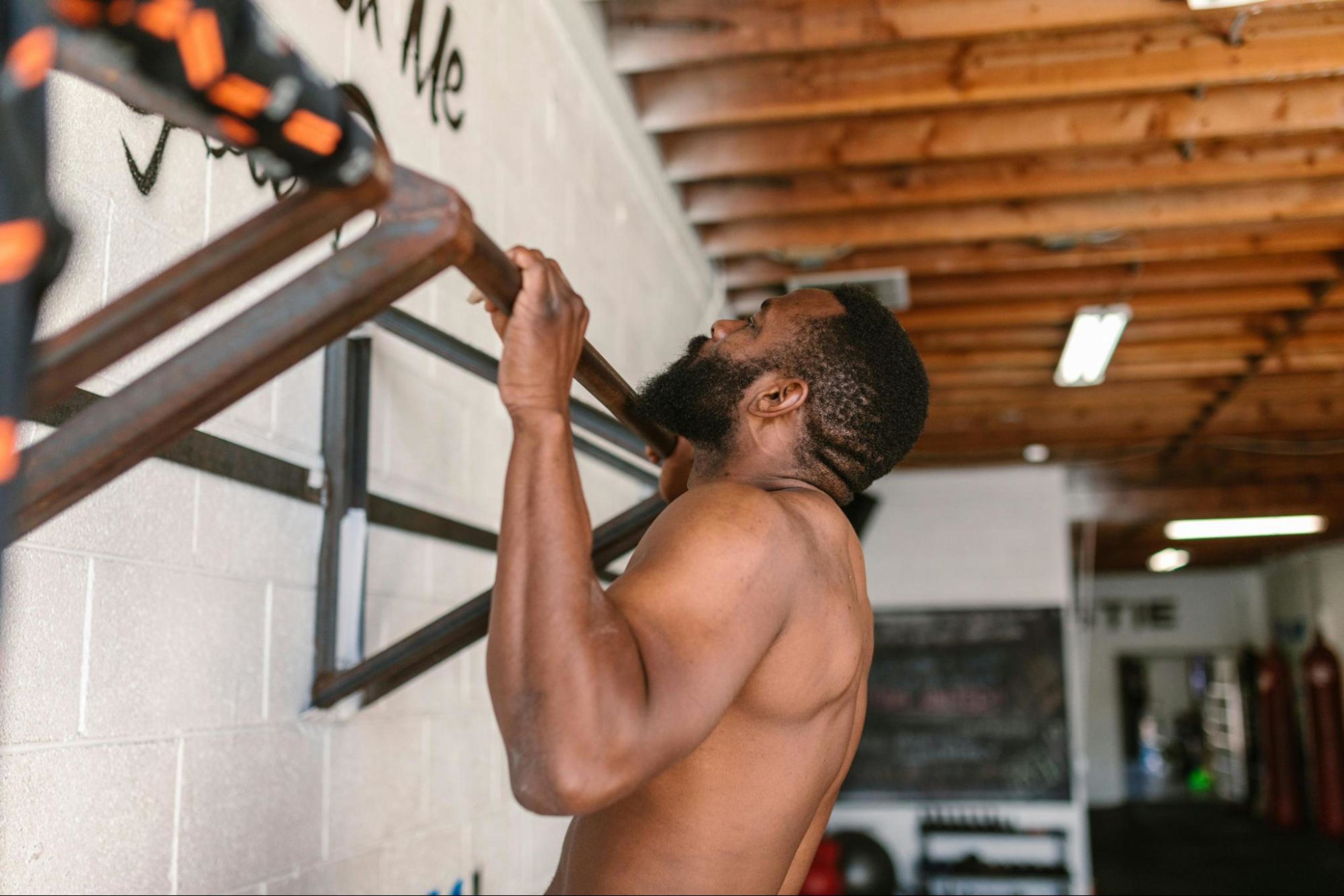 Man does pull-ups in a gym after learning about split vs. full-body training.