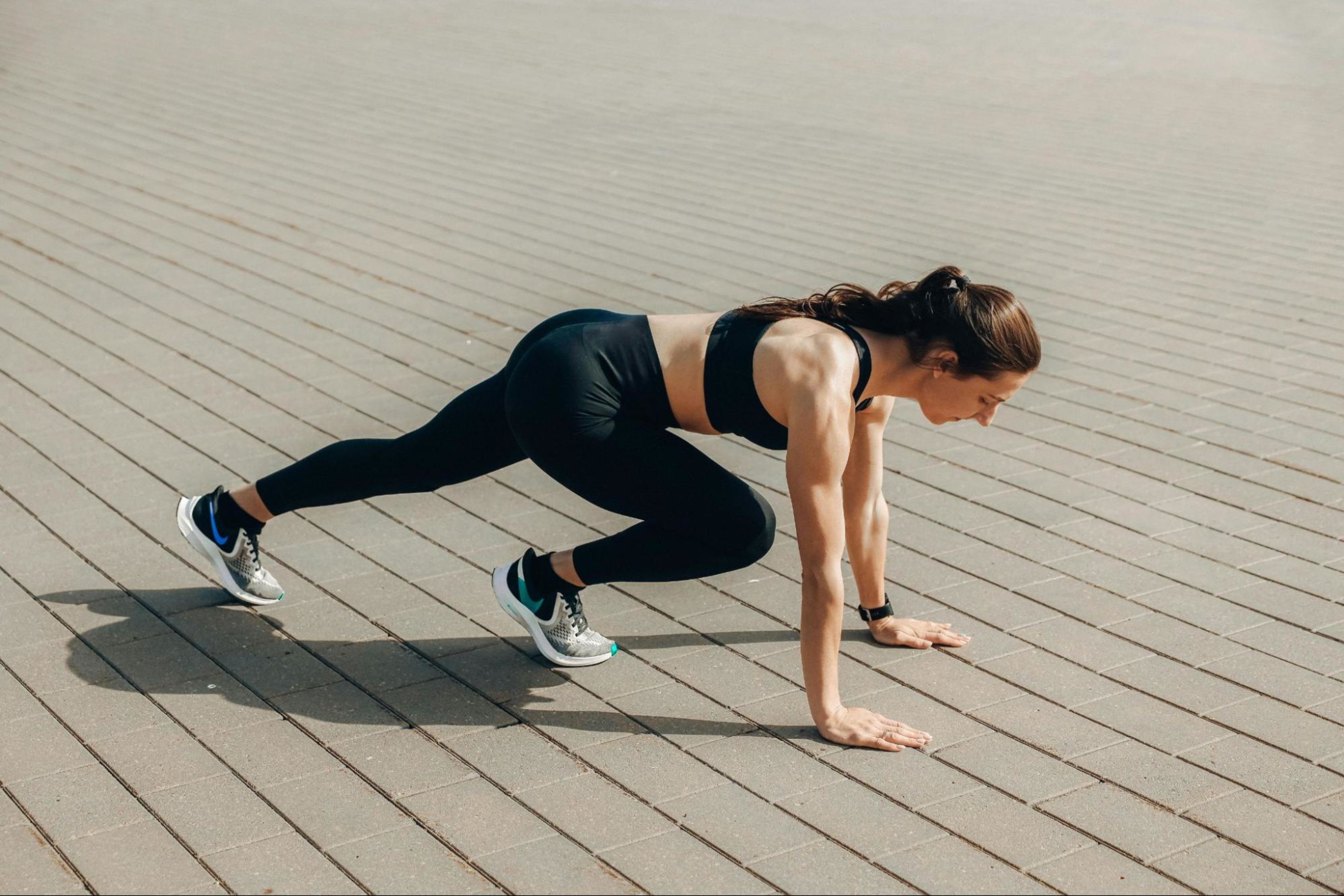 Woman does strength training postpartum to get in shape by doing mountain climbers outdoors.