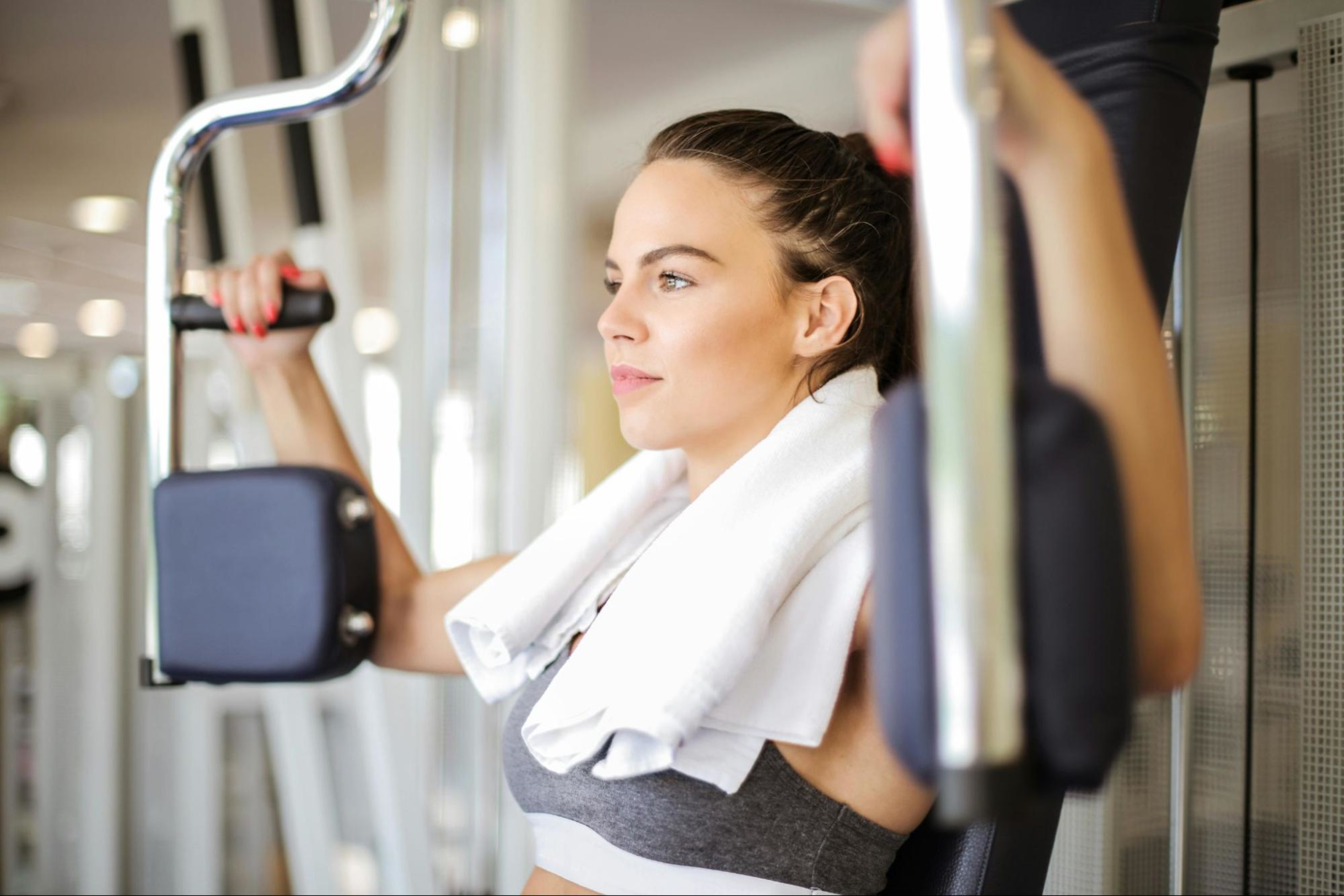 Woman follows a postpartum strength training program by doing an arm workout at the gym.